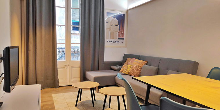 Unwind in the living area, where modern furnishings meet classic Barcelona charm with a small balcony overlooking the street.