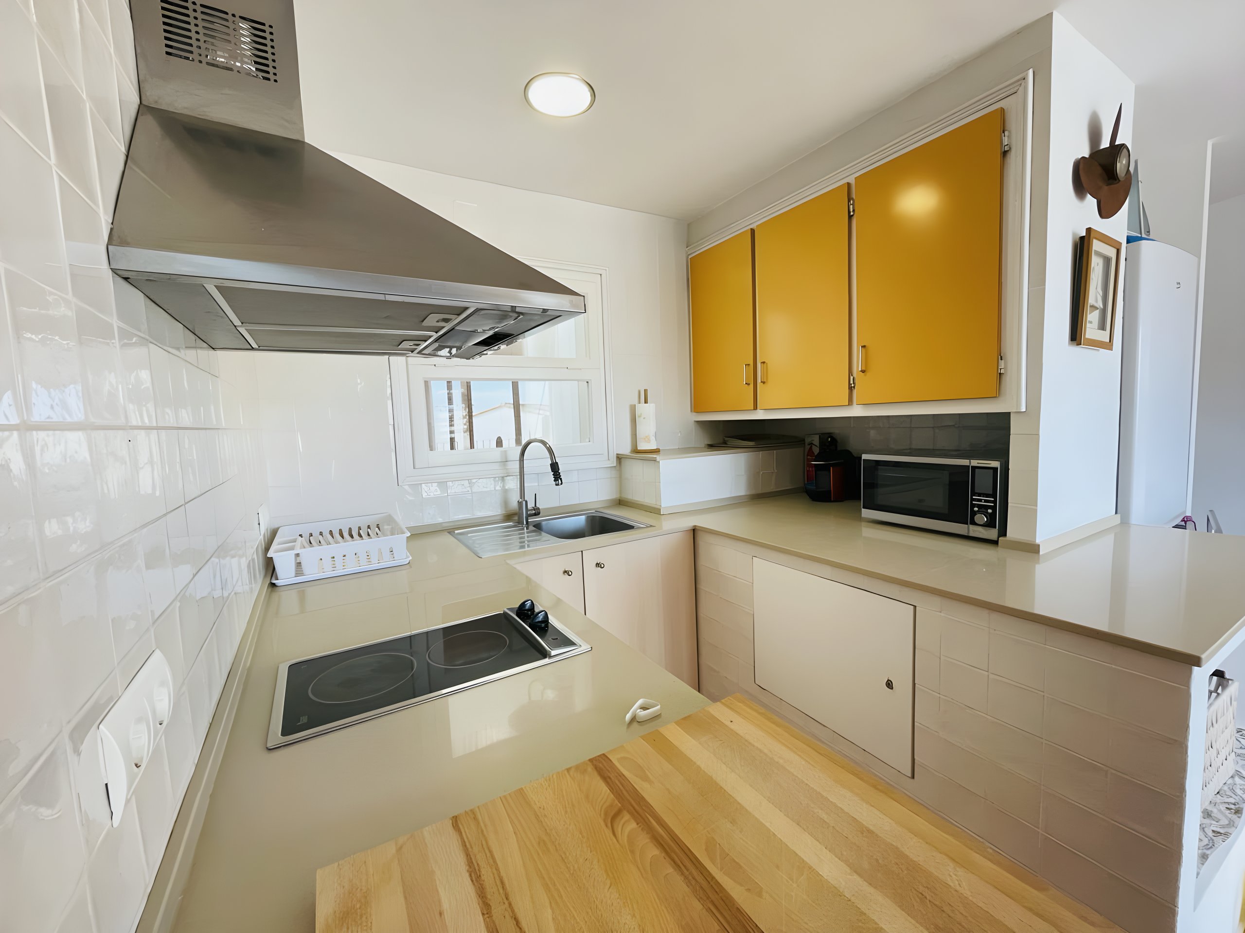 The modern kitchen features a stainless-steel stovetop and a sleek, stainless-steel range hood. It is equipped with a microwave oven and ample cabinetry. The kitchen has a window that provides natural light, making the space bright and airy. The counter space is ideal for food preparation and dining, and the warm wood countertop adds a touch of rustic charm.