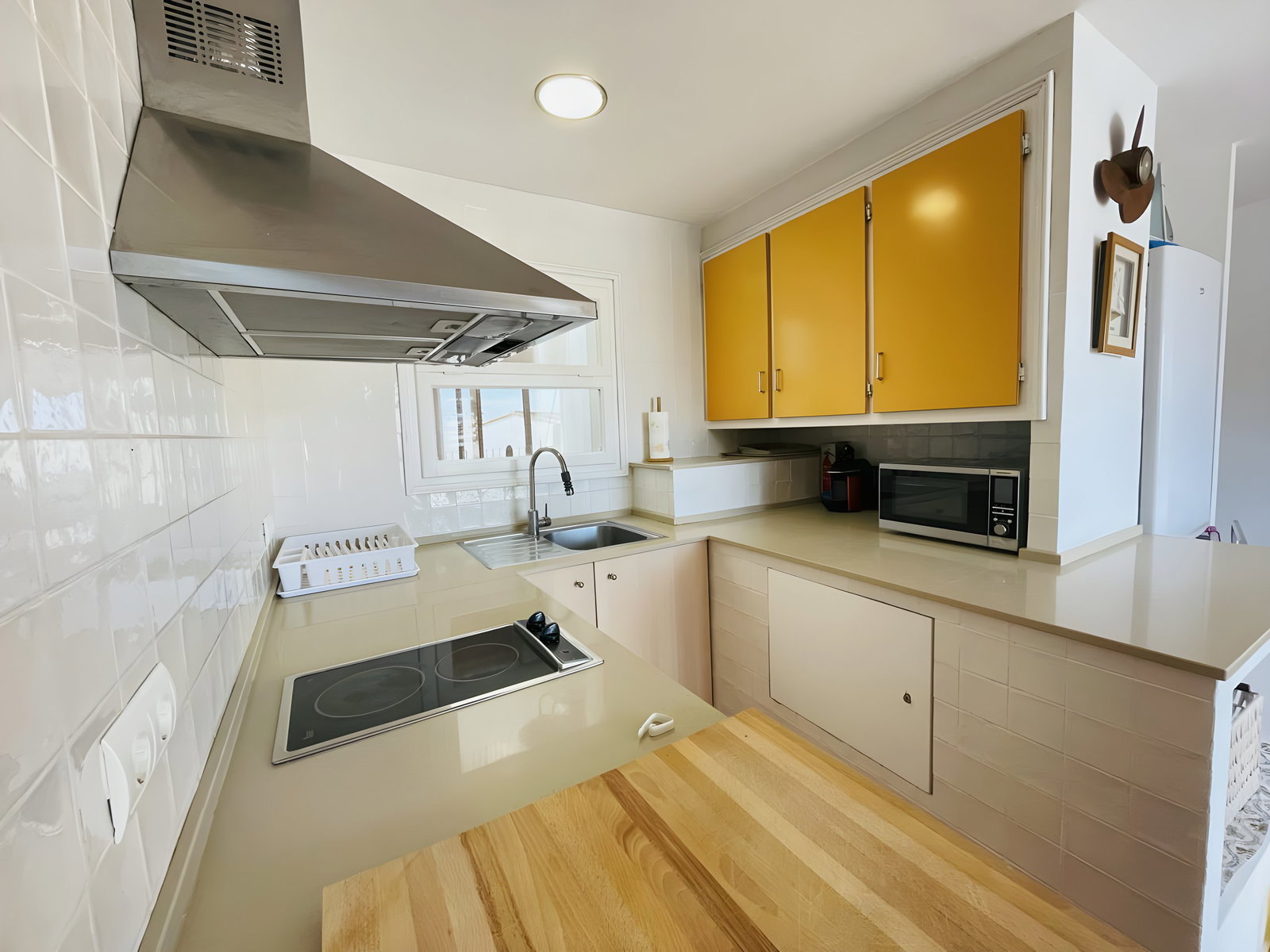 The modern kitchen features a stainless-steel stovetop and a sleek, stainless-steel range hood. It is equipped with a microwave oven and ample cabinetry. The kitchen has a window that provides natural light, making the space bright and airy. The counter space is ideal for food preparation and dining, and the warm wood countertop adds a touch of rustic charm.