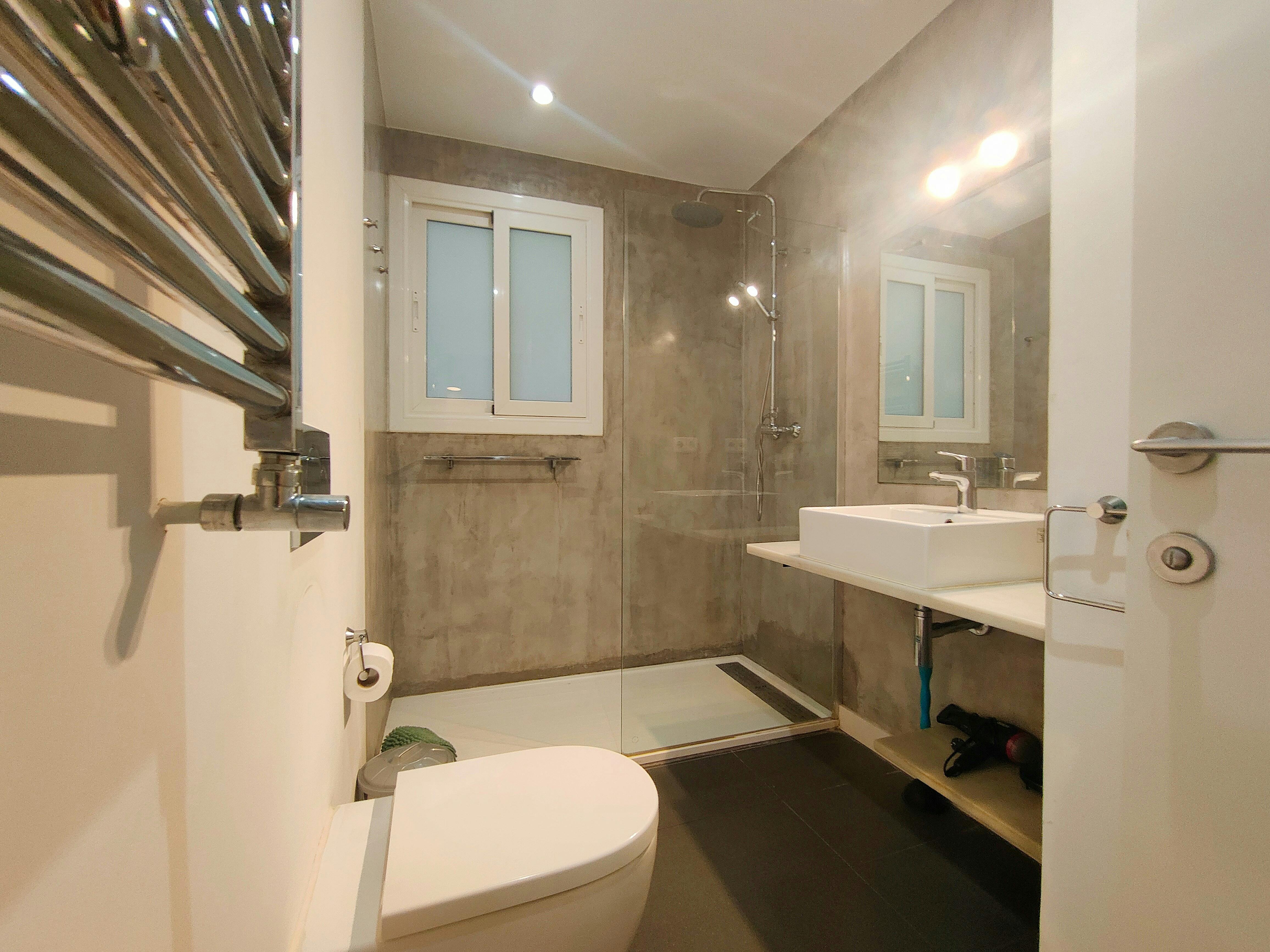 This bathroom features a modern, minimalist design with a large walk-in shower, a sleek white sink and a  toilet. The shower boasts a glass enclosure and a towel rail.
