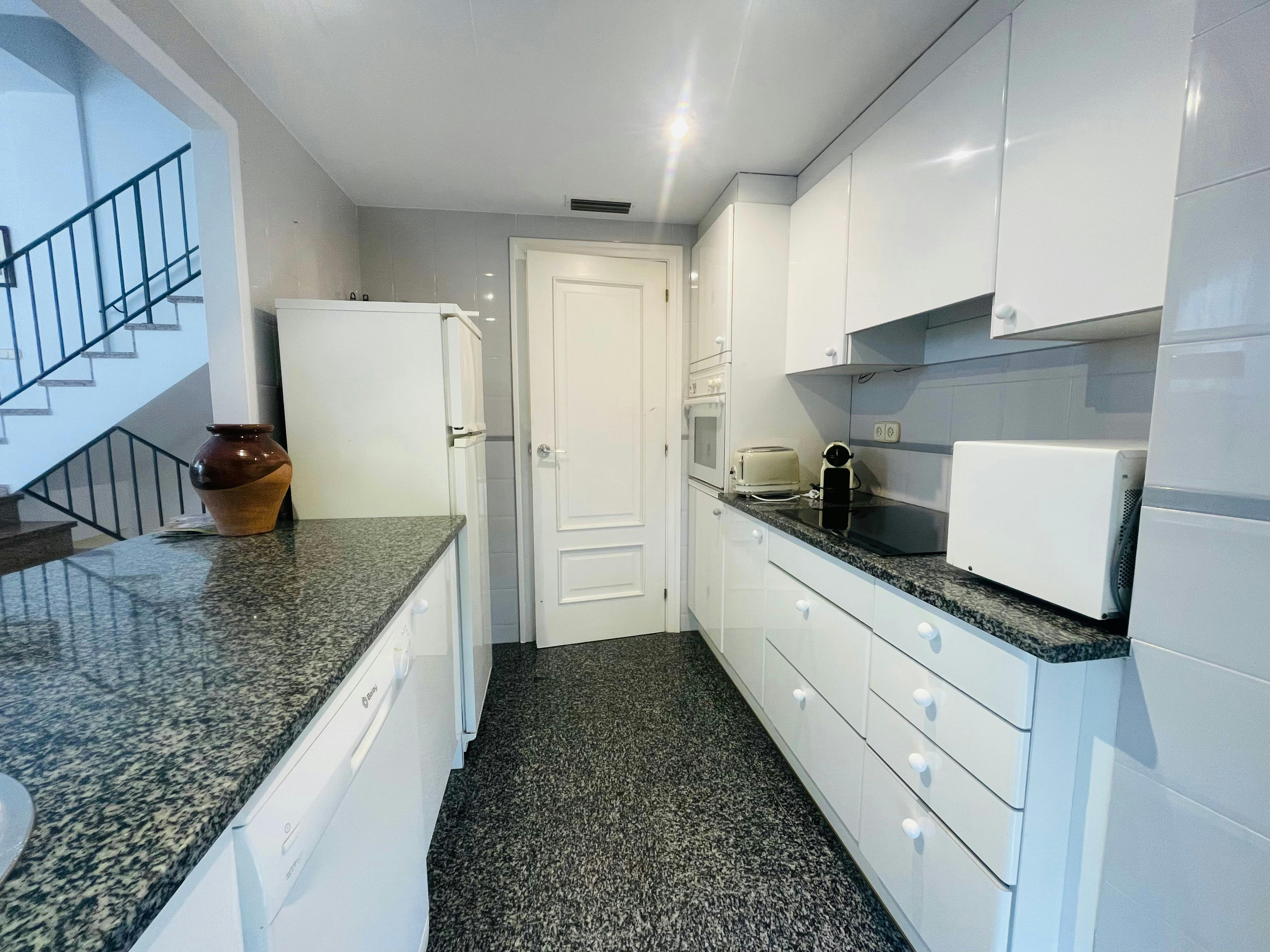 This modern kitchen features sleek white appliances and generous dark granite countertops, providing a stylish and efficient space for meal preparation.