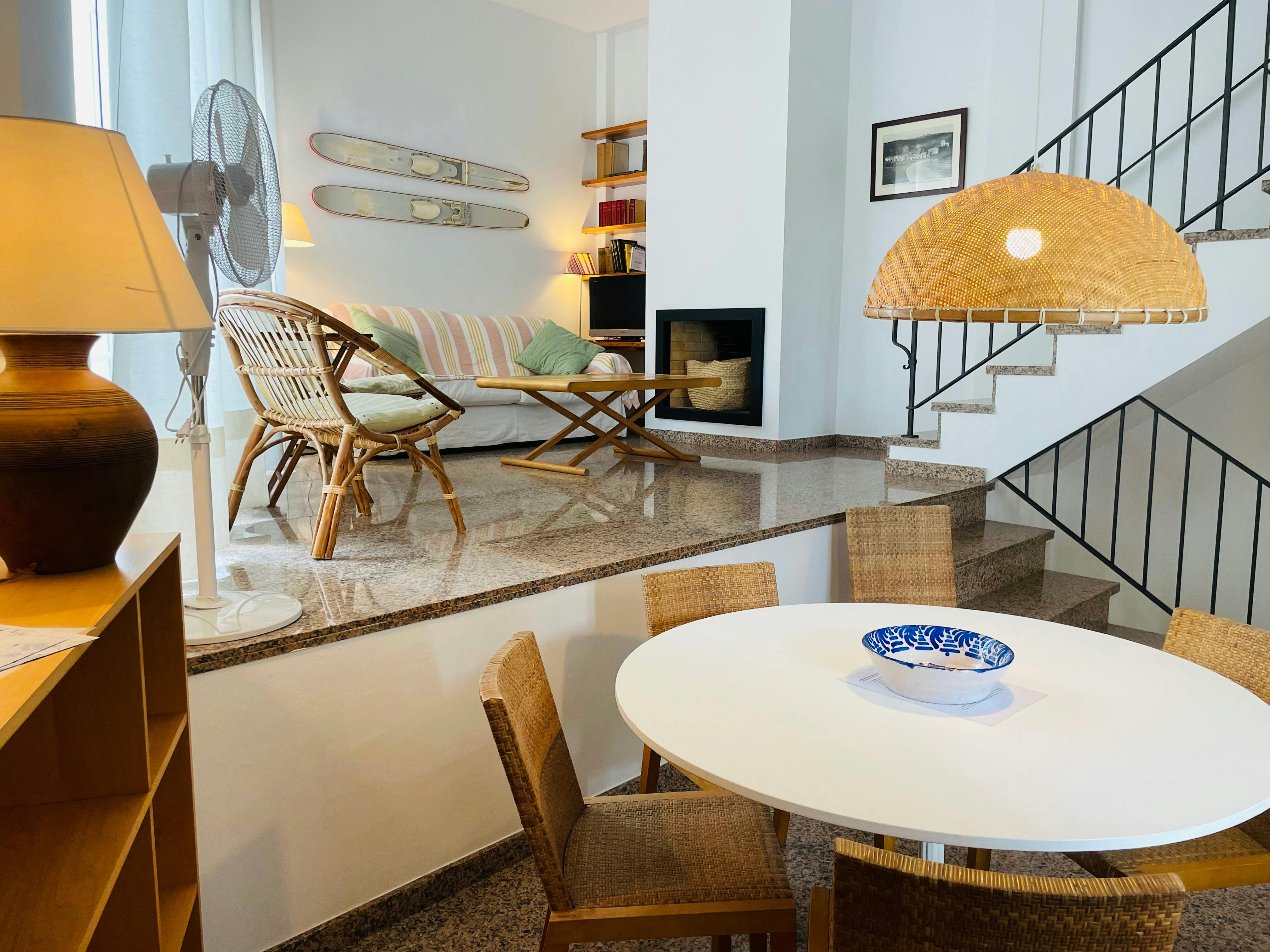 Natural light illuminates the split-level design of this inviting townhouse, highlighting the warm tones of the wicker furniture and polished stone floor.