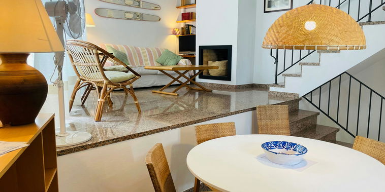 Natural light illuminates the split-level design of this inviting townhouse, highlighting the warm tones of the wicker furniture and polished stone floor.