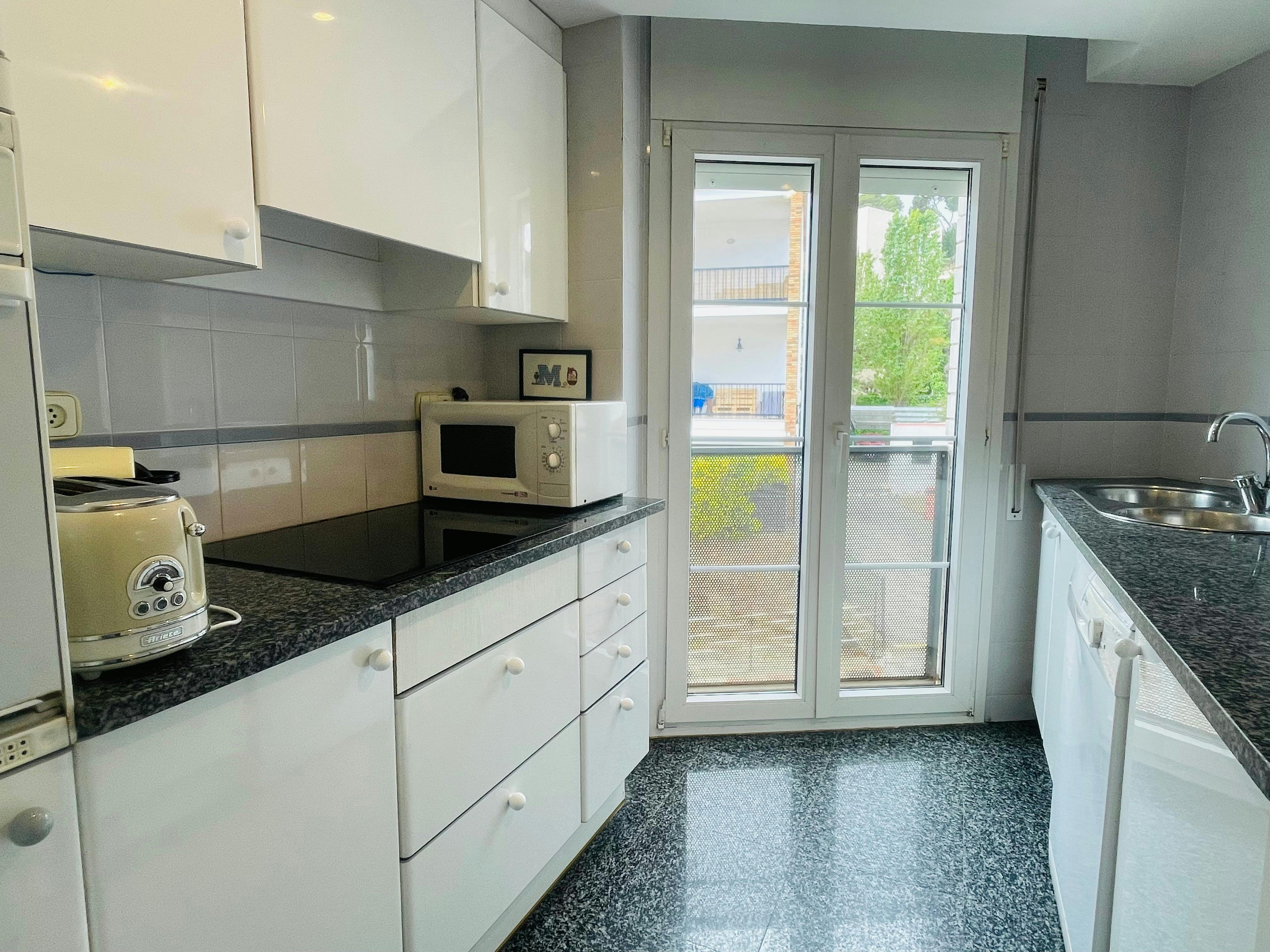 This bright, fully equipped kitchen boasts modern white cabinetry and dark granite countertops, offering a stylish and functional space for preparing meals.