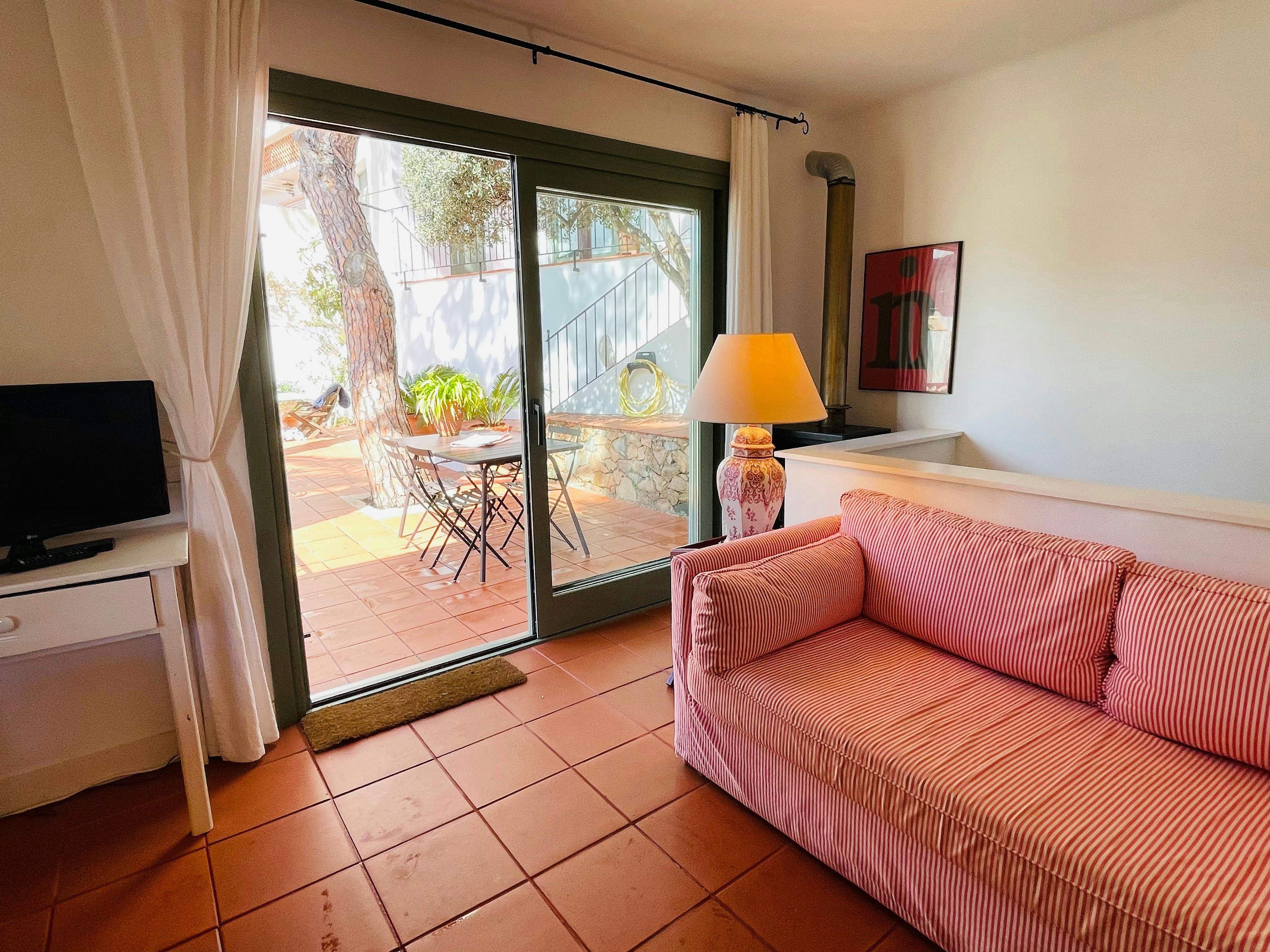 The living room is bright and airy, with large glass doors that open onto a private patio.  The patio features a table and chairs, perfect for enjoying meals outdoors. The  tiled floor adds a touch of traditional Spanish charm.