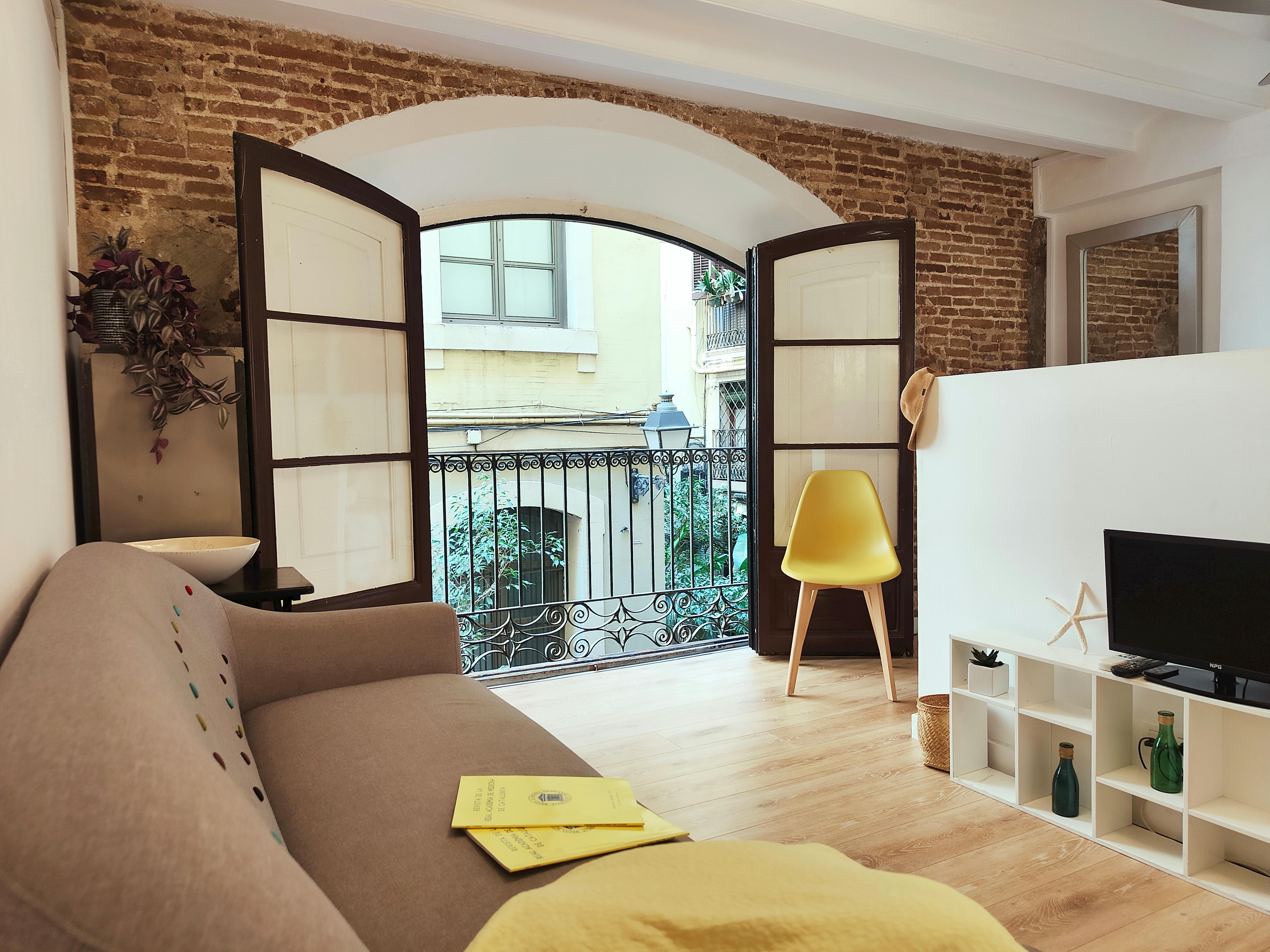 The living area features a comfortable sofa, perfect for relaxing after a day of exploring Barcelona. The large windows open to a charming street (Passatge), allowing natural light to flood the space.