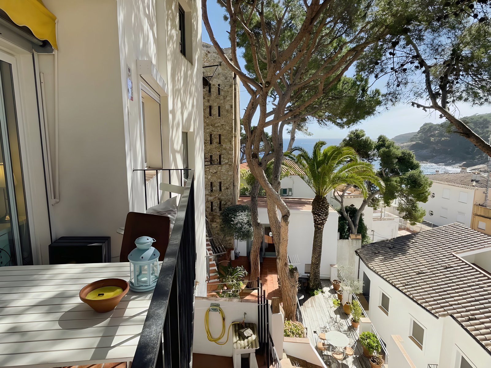 This photo shows the private balcony of the apartment, with a table and chairs, perfect for enjoying a morning coffee or an evening glass of wine while taking in the stunning views of the surrounding village, the Mediterranean Sea, and the lush greenery.  The balcony is just off the living room and is accessible through sliding glass doors.
