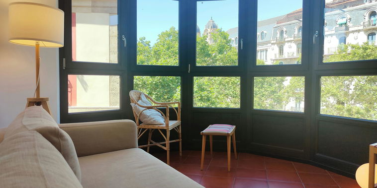 The living room is bathed in natural light streaming through a large bay window offering stunning views of the city.