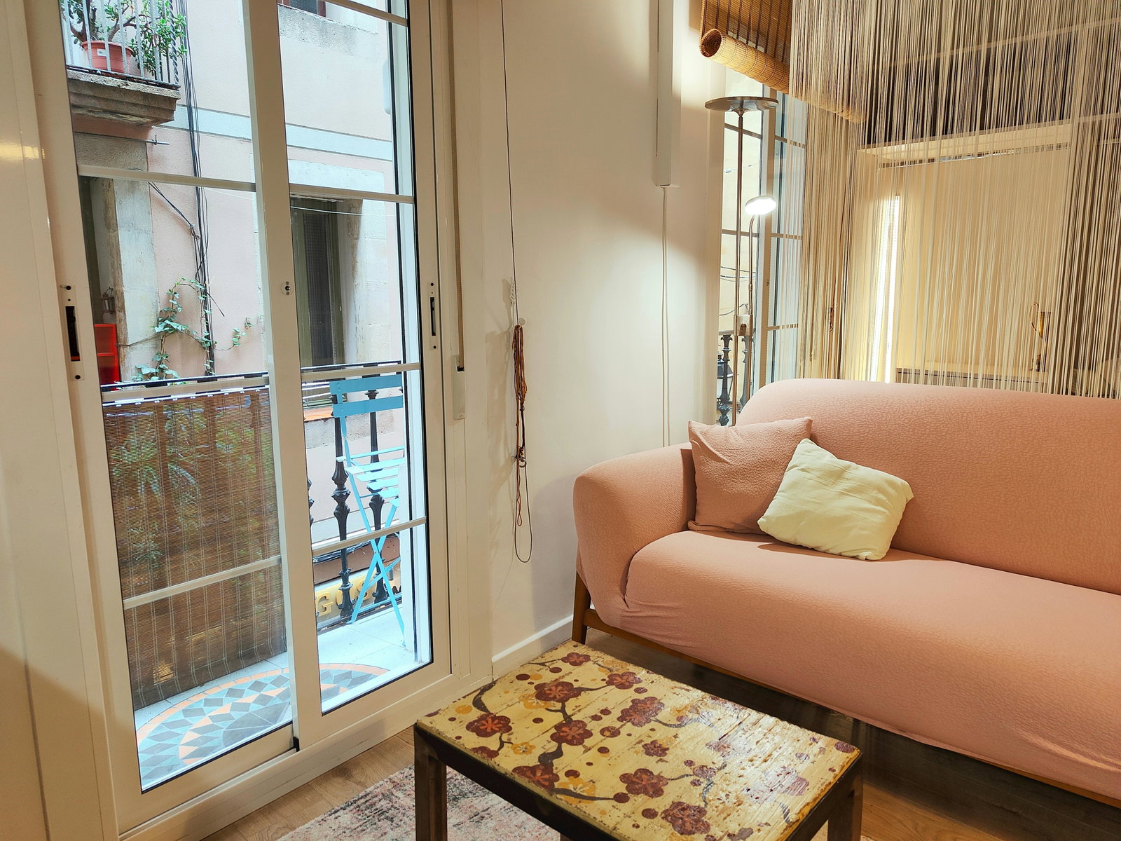 Natural light streams into this trendy Barcelona loft, illuminating a stylish living space designed for relaxation and urban exploration. The blend of modern furnishings and glimpses of traditional Spanish architecture through the balcony door creates a unique and inviting ambiance.