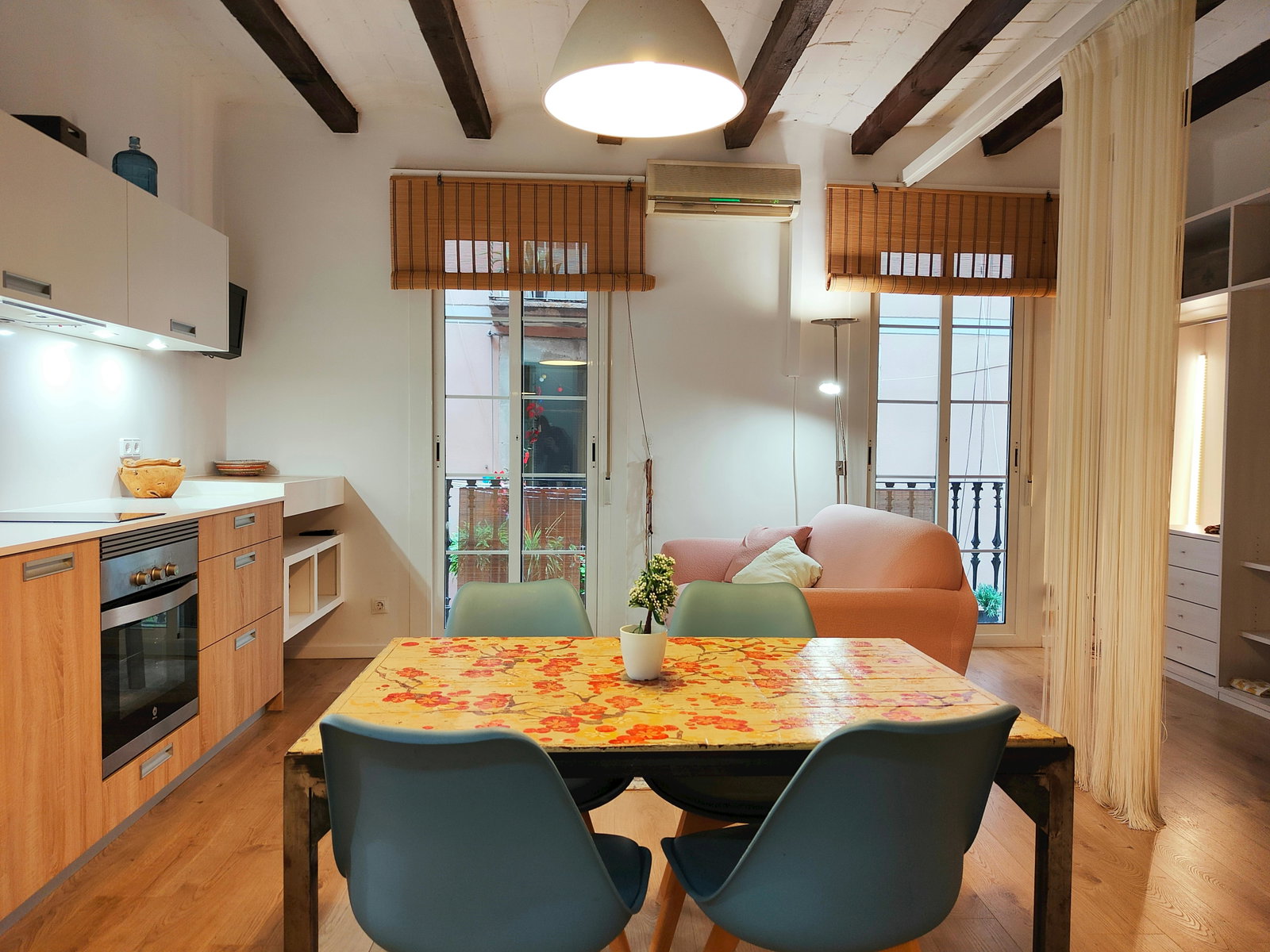 The dining area features a wooden table surrounded by four chairs.  A glimpse of the modern kitchen can be seen in the background, with its wooden cabinets and sleek appliances.