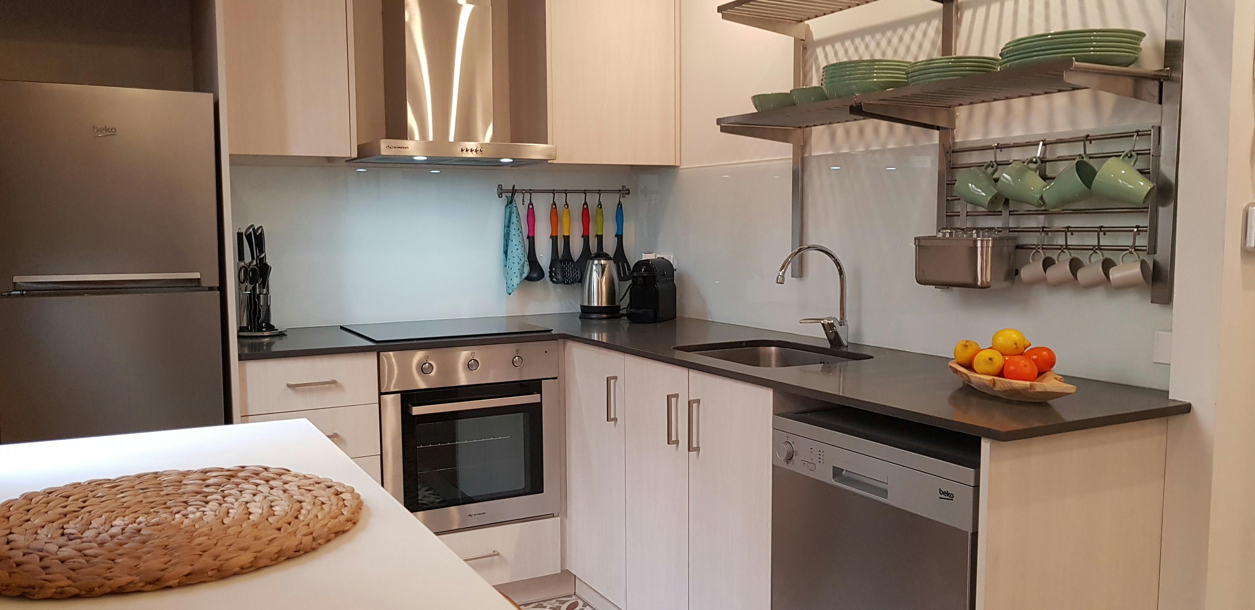 This is a view of the living room, featuring a light blue sofa with patterned cushions and a white side table with a candle. The room is tastefully decorated with minimalist furniture and an exposed brick wall.  A doorway leads into the bedroom, which features a queen-sized bed and a small desk.  The living room also includes a dining table with two chairs. There's also a window with a view of the city.  The overall ambiance of the room is bright and modern, with a touch of warmth.