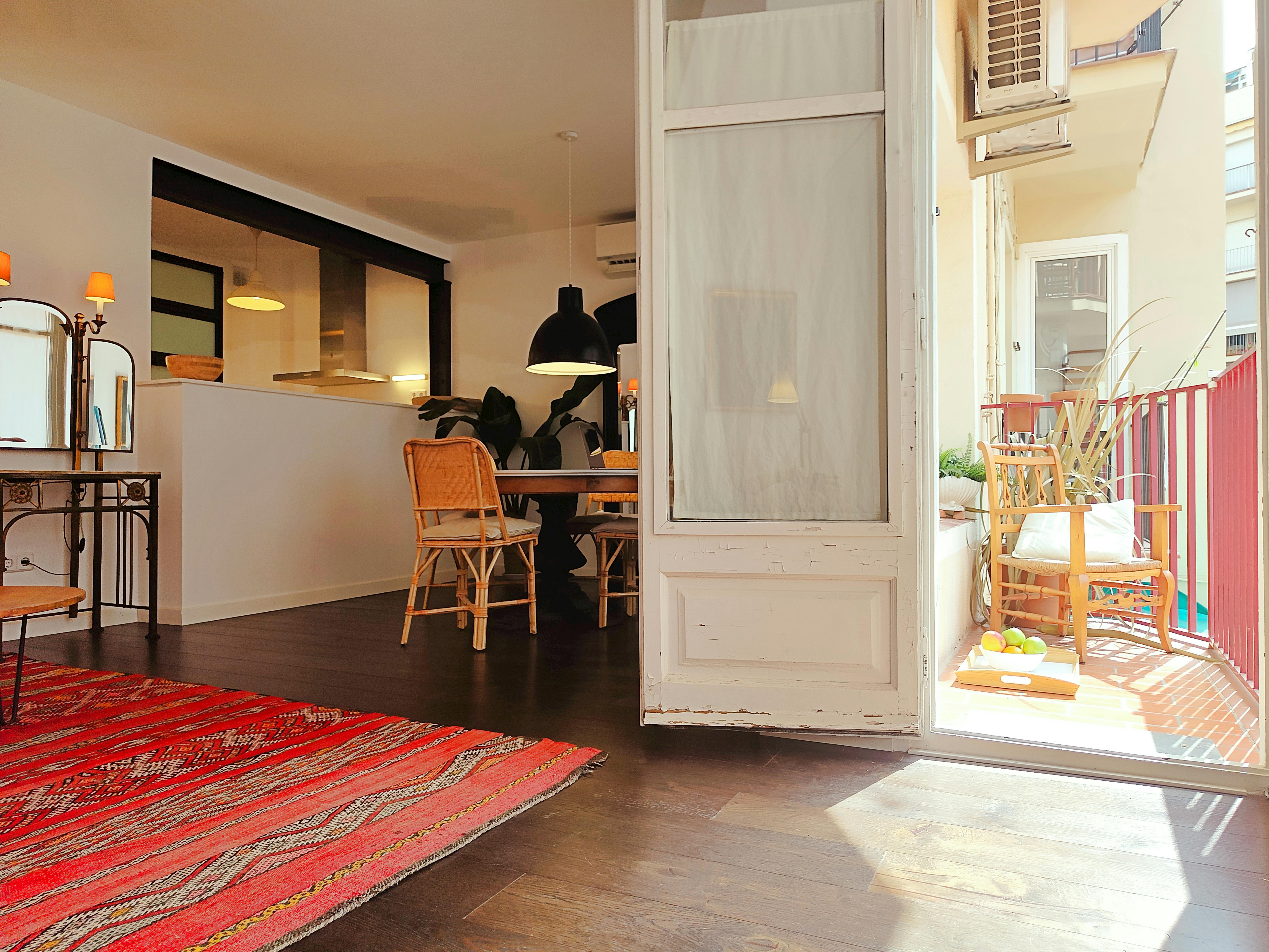 The apartment features a charming, sunlit living area with wooden floors and a vibrant red patterned rug. Small private terrace.