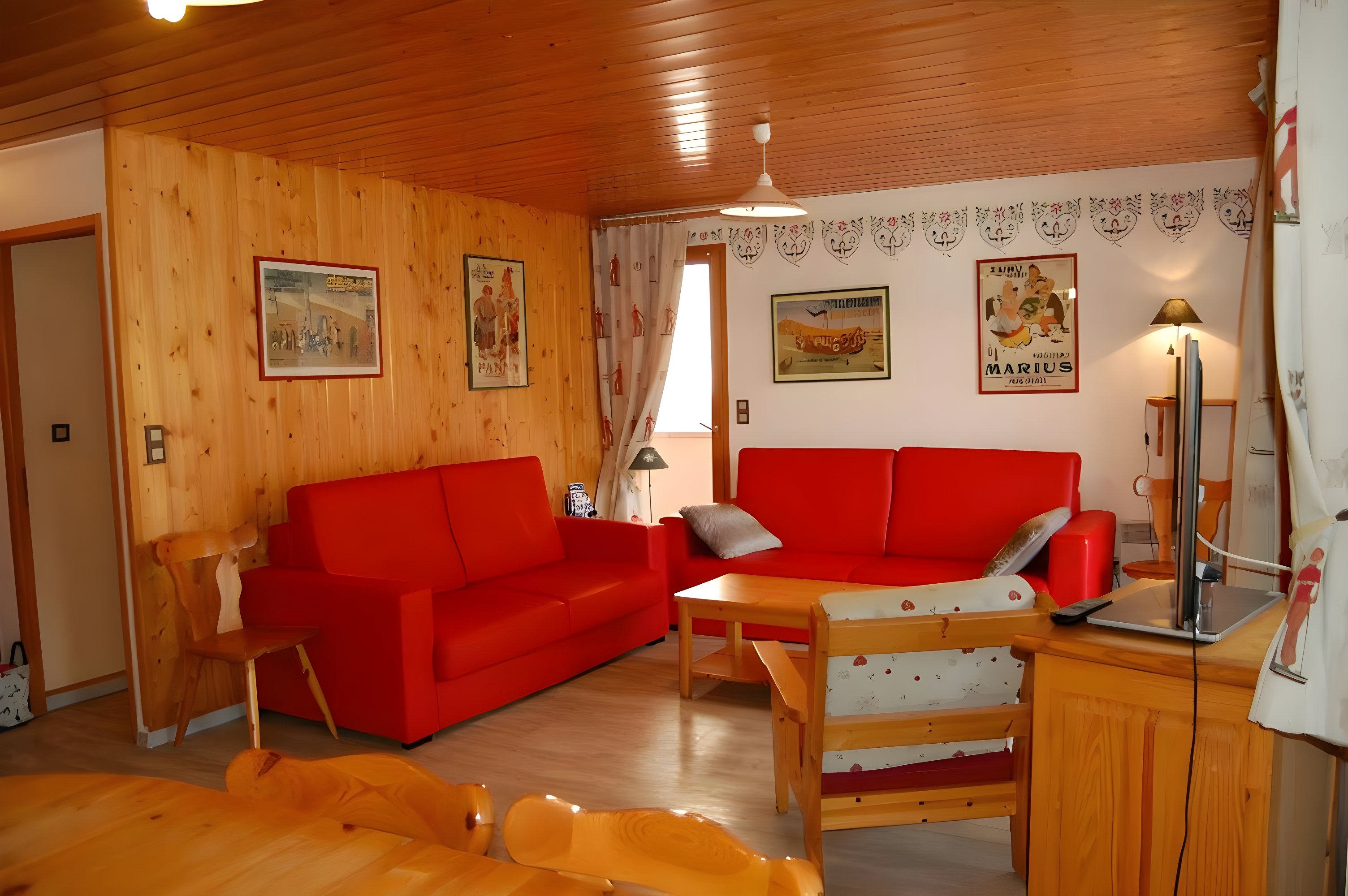 This inviting bedroom features a double bed with a light yellow duvet and a wooden headboard. The room is decorated in a traditional style, with a floral wallpaper border and a framed painting depicting a bouquet of white flowers in a blue vase. Natural light streams in from the window, highlighting the room's cozy and comfortable atmosphere.