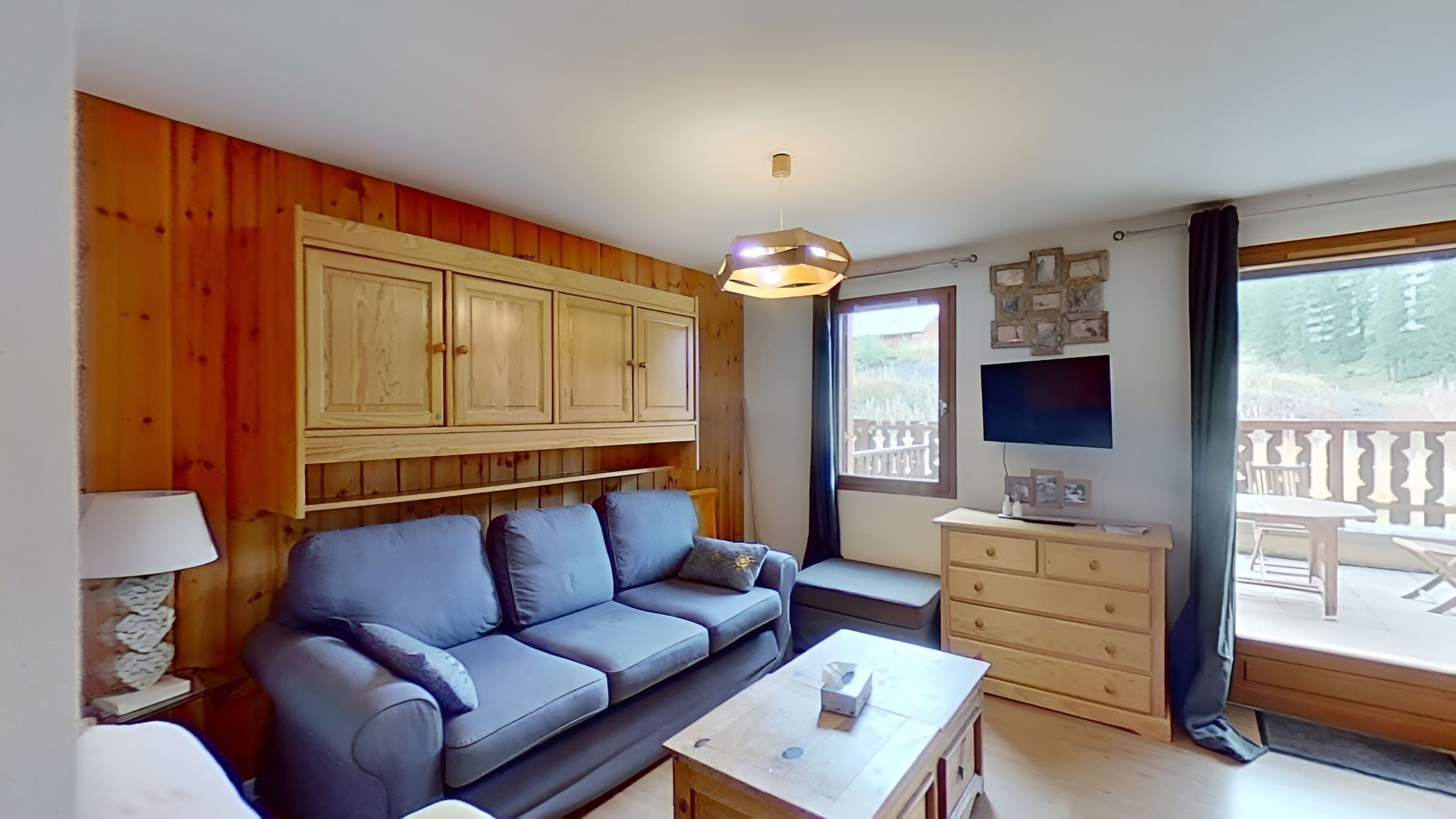 The balcony features a wooden table and chairs, providing a comfortable spot to enjoy the breathtaking mountain views. The surrounding mountains, covered in lush greenery, create a picturesque backdrop. The balcony is enclosed by a wooden railing, ensuring privacy and security.  This is a great spot to unwind after a day of exploring the area.