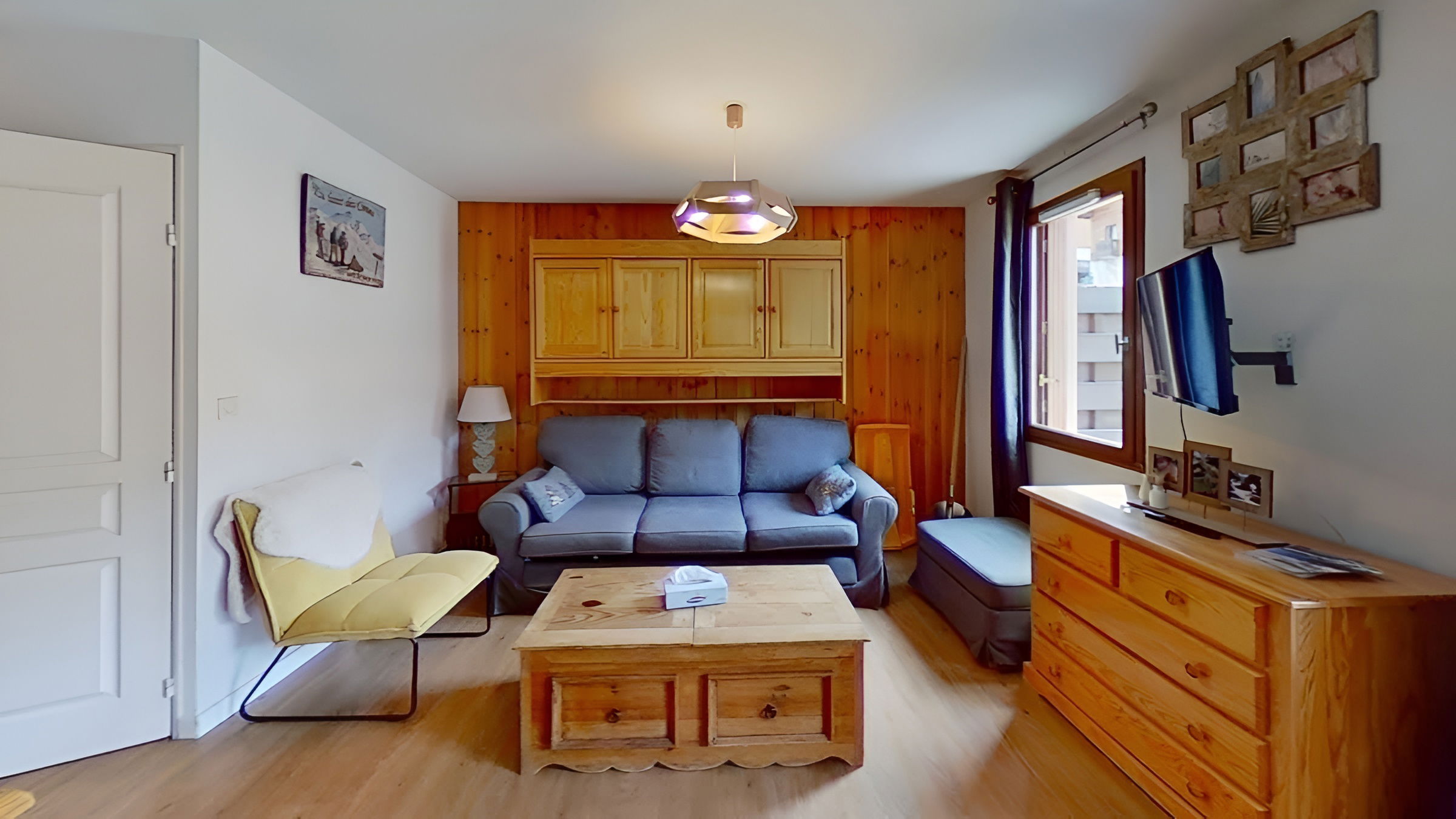 This inviting living area features a comfortable sofa, a coffee table, and a flat-screen TV. Sliding doors lead to a private terrace with a view of the surrounding mountain landscape.  The warm wood paneling on the walls adds a touch of rustic charm to the space, while the large windows provide plenty of natural light.