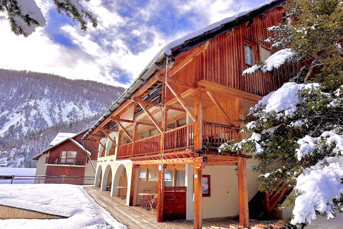The exterior of the building features a charming wooden facade, with a snow-covered roof and a balcony overlooking the snowy landscape. The building's architecture blends seamlessly with the alpine surroundings, offering a picturesque setting for a peaceful and relaxing getaway.