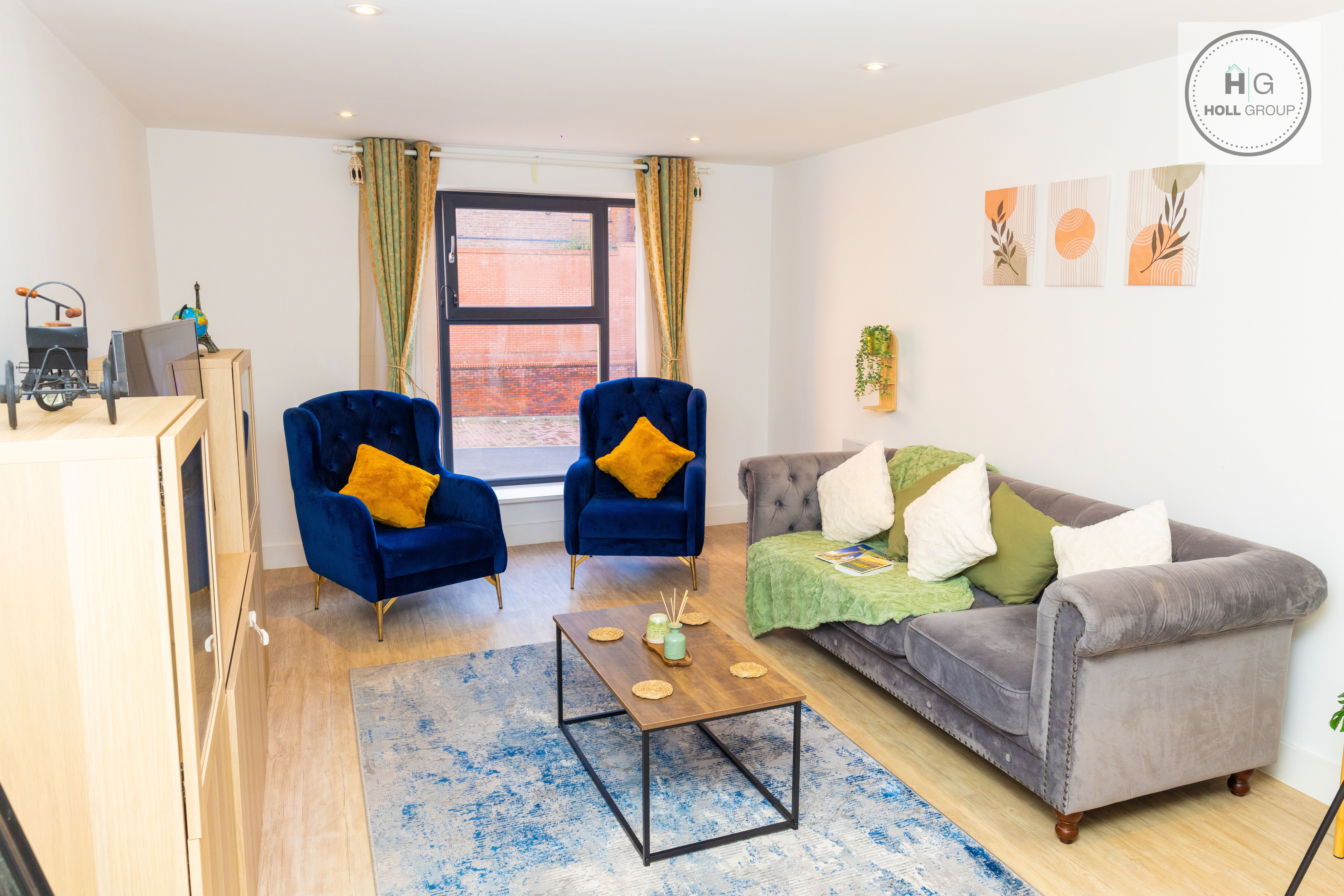 A spacious, beautifully designed living room with a cosy sofa, two velvet armchairs and warm lighting. Large windows bring in natural light, and the room’s modern décor creates a calm, comfortable atmosphere that makes you feel instantly at home.