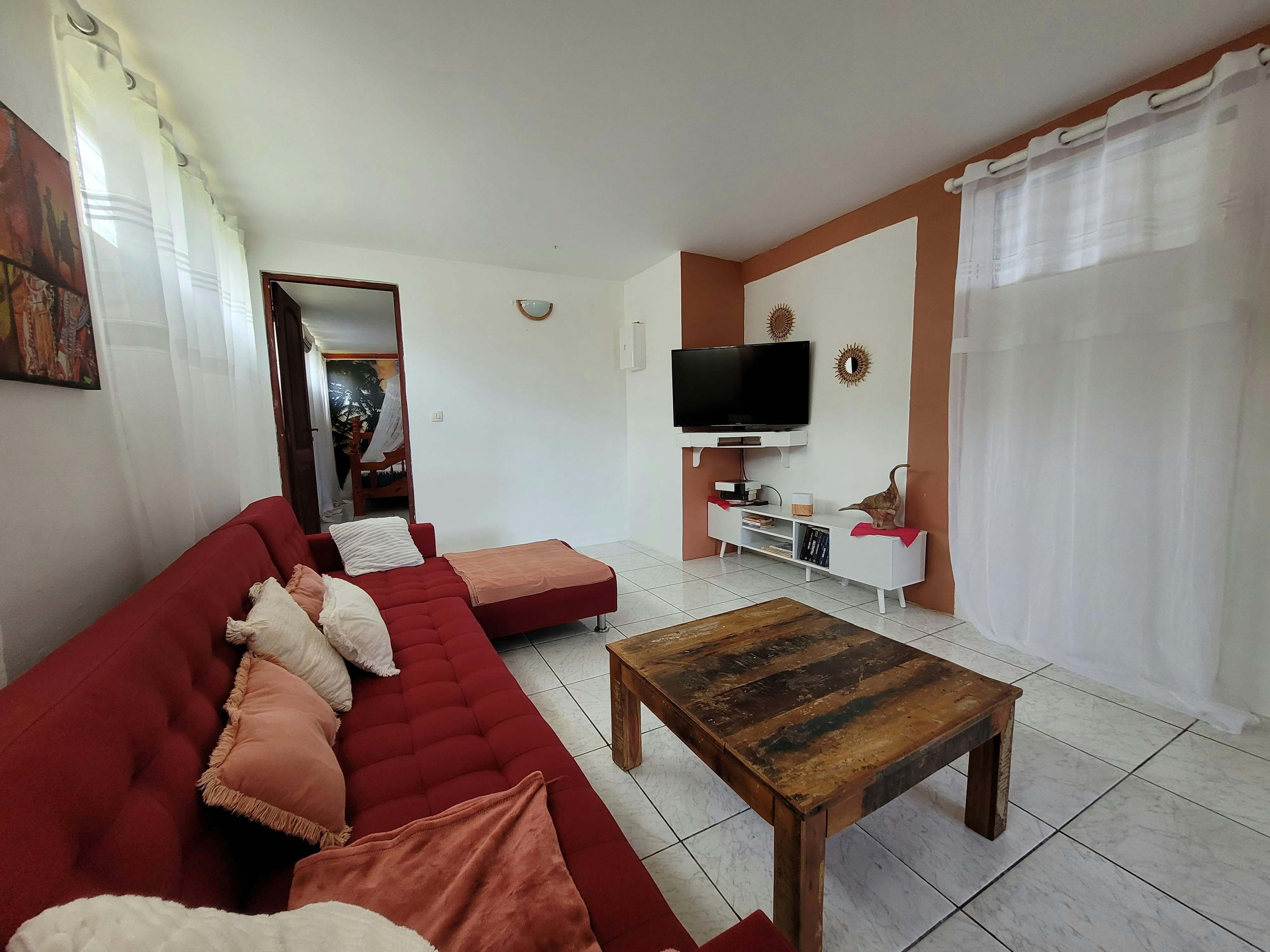 Salon cosy avec grand canapé d’angle, TV connectée pour vos soirées détente, et une sélection de livres à disposition pour tous les goûts.