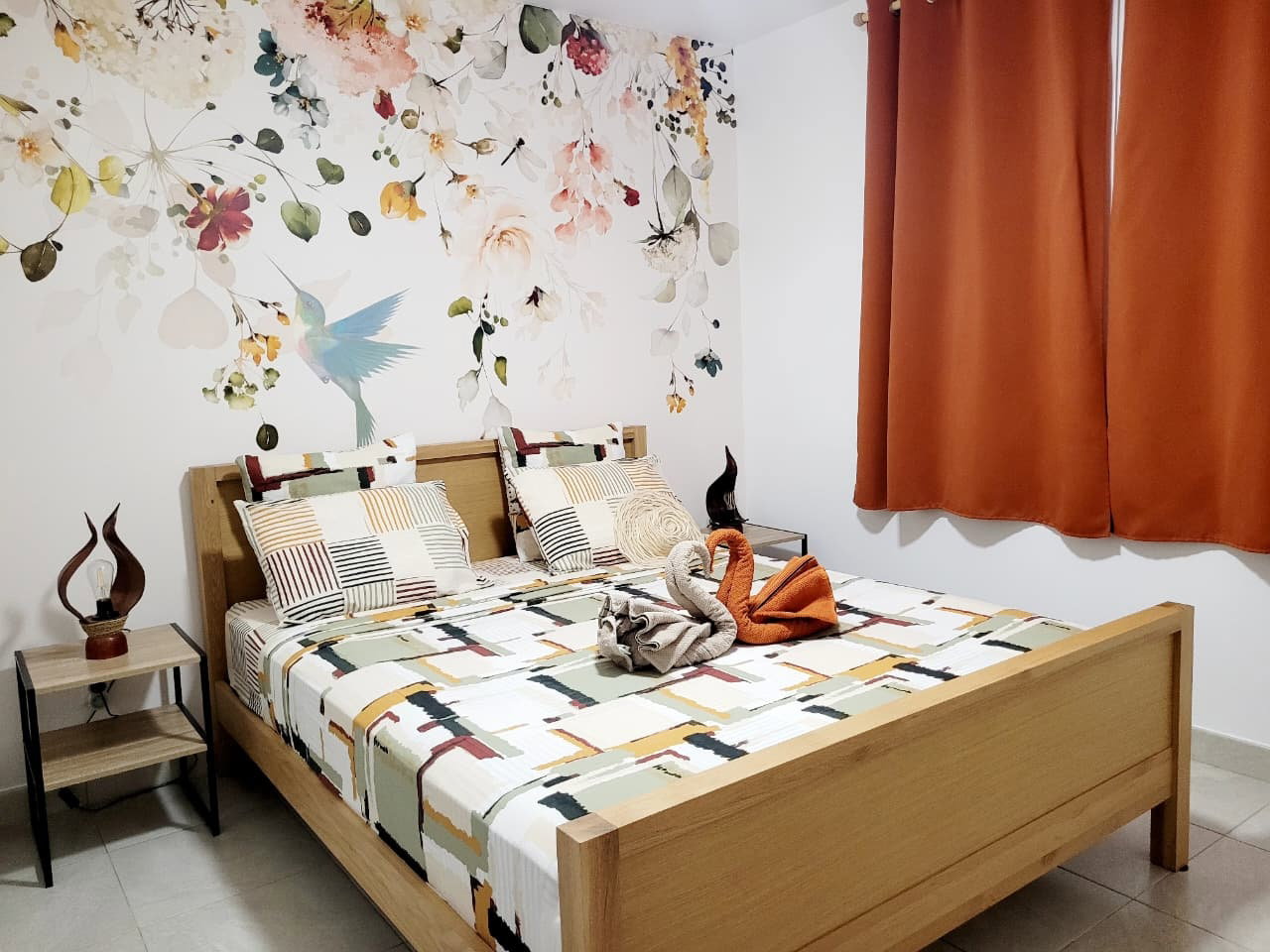 CHAMBRE 1 : Chambre cosy avec lit en 160, table de nuit et lampes de chevet pour une ambiance chaleureuse. Climatisation et ventilateur complètent le confort.