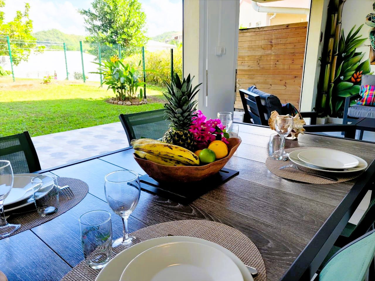 Coin repas extérieur sur terrasse couverte, avec table et quatre chaises, idéal pour partager vos repas tout en profitant du jardin et de la fraîcheur de l’air.