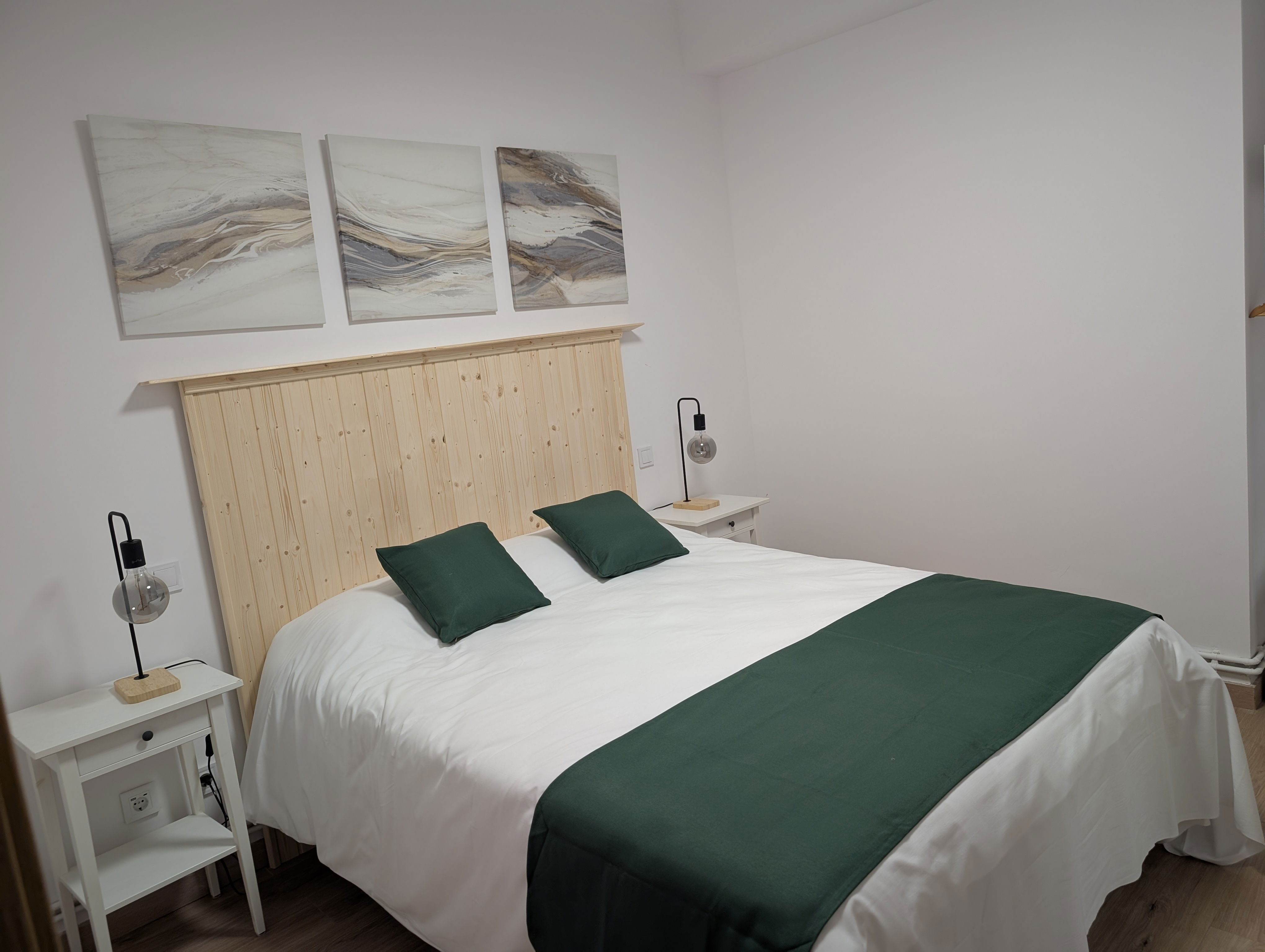 Retreat to this serene bedroom, where a natural wood headboard and soothing green accents create a tranquil atmosphere. Modern lighting and abstract art add a touch of contemporary style to ensure a restful night's sleep.