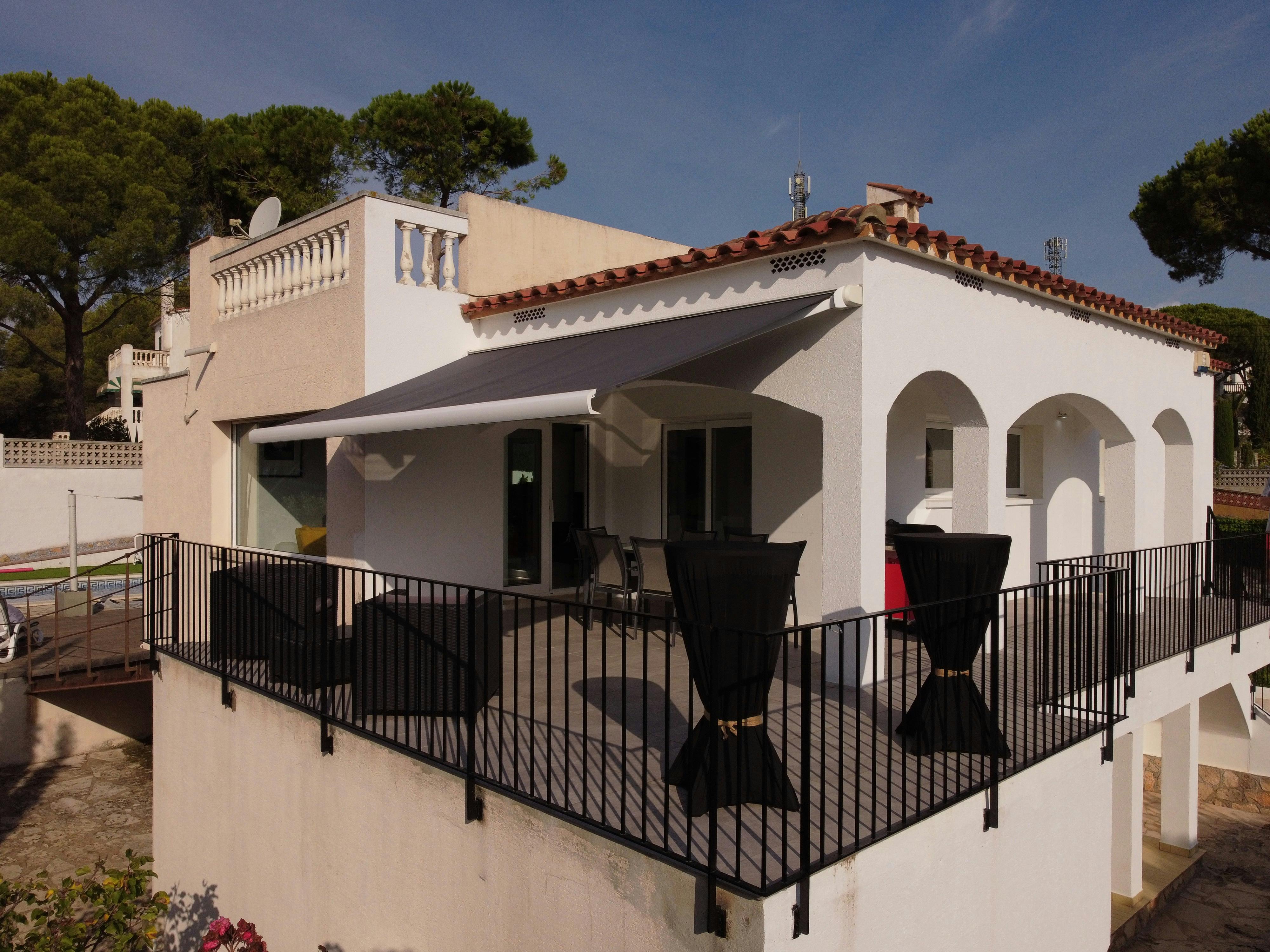 This white villa boasts an elevated terrace with classic archways. A sleek awning invites relaxed outdoor dining.