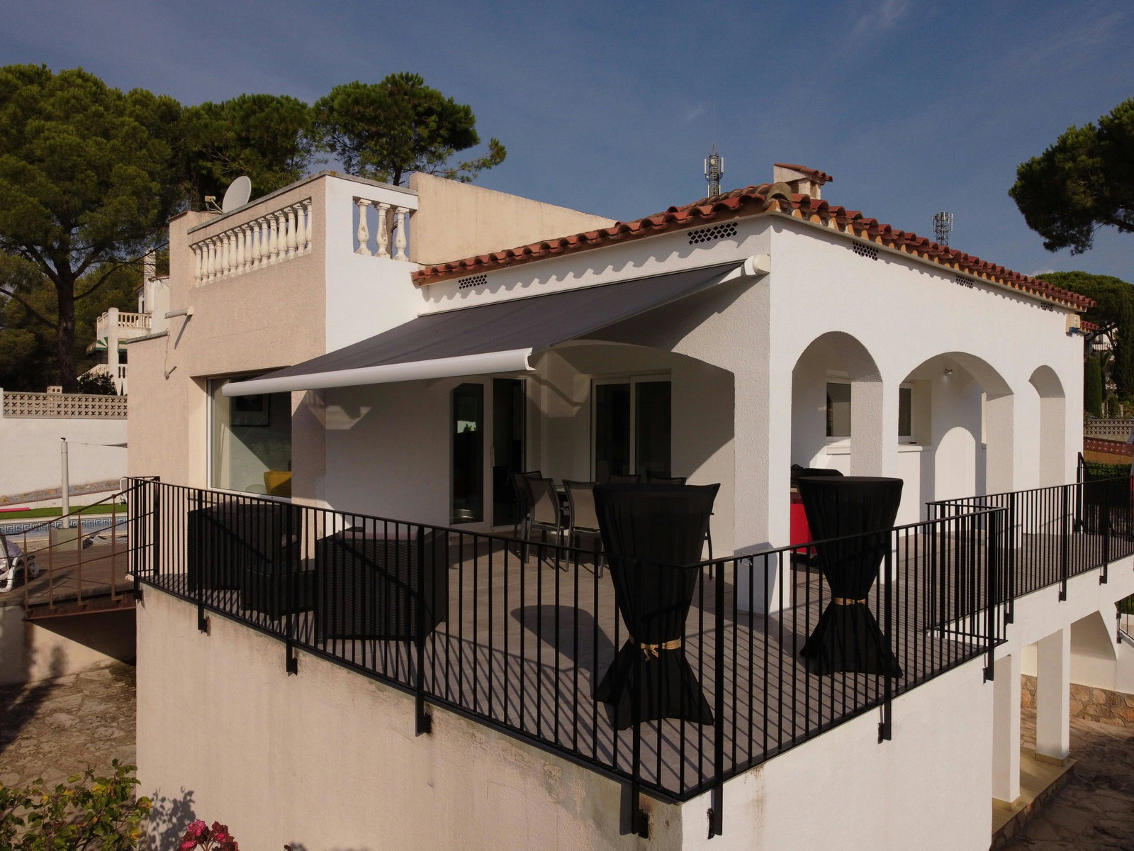 Diese weiße Villa besticht durch eine erhöhte Terrasse mit klassischen Torbögen. Eine elegante Markise lädt zu entspannten Mahlzeiten im Freien ein.