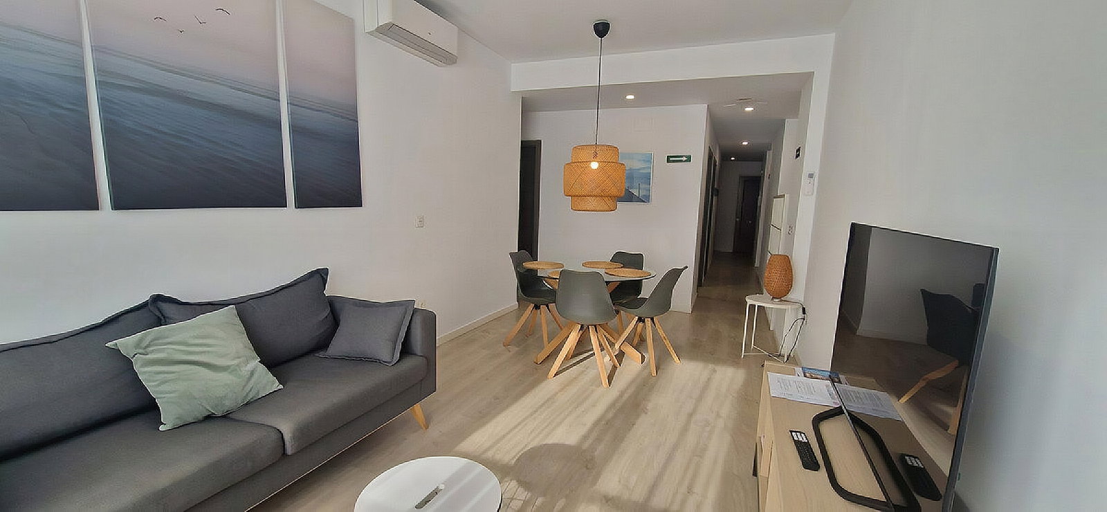Relax in the bright, modern living area, featuring clean lines, light wood floors, and a stylish woven pendant lamp.