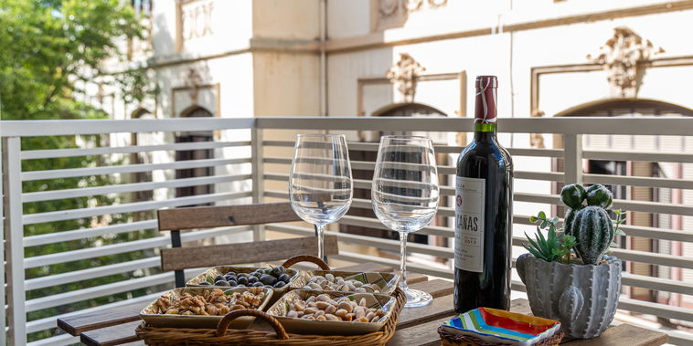 Savor wine and snacks on the wooden balcony table. Ornate historic facades offer a charming backdrop.