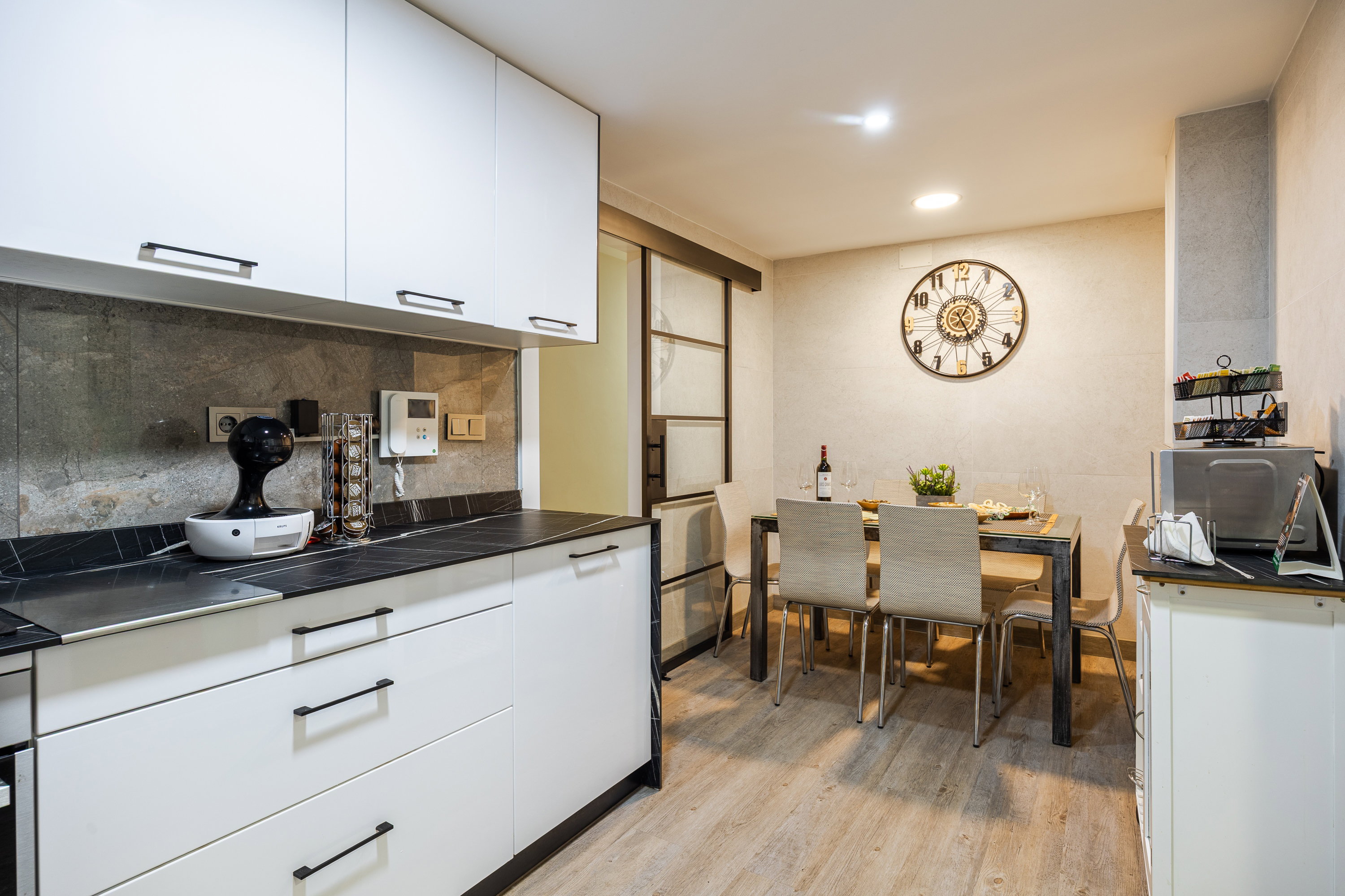 A fully equipped kitchen features sleek white cabinetry and black countertops. The adjacent dining area offers a cozy retreat.