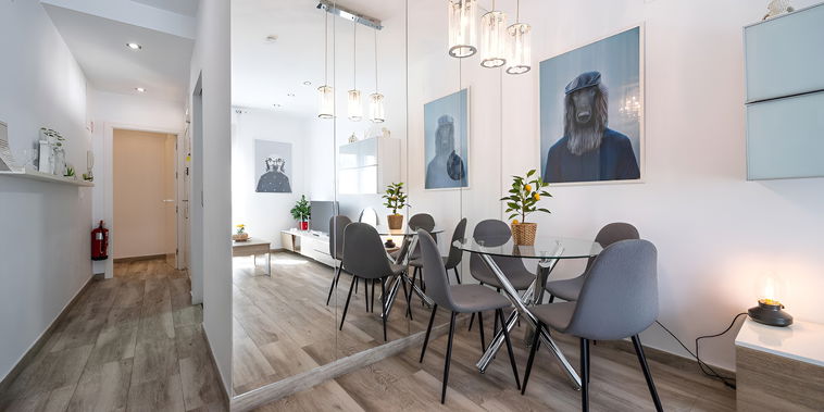 The living room/tv room is open to the dining area, which features a table with four chairs and a large mirror.