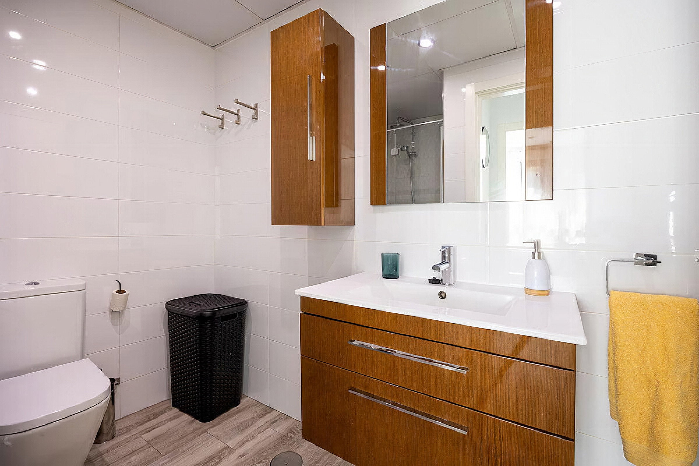The bathroom is equipped with a small toilet, a sink with cabinets, a mirror, a trash can, towels, and towel racks.