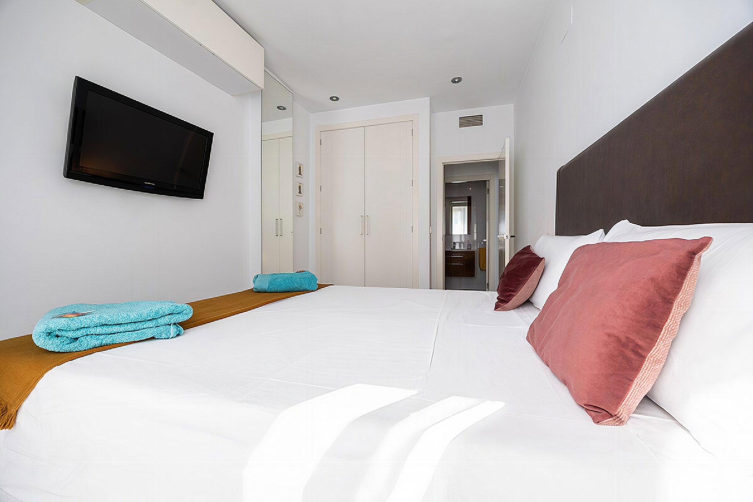 The bedroom has a wardrobe, a TV, and a queen-size bed.