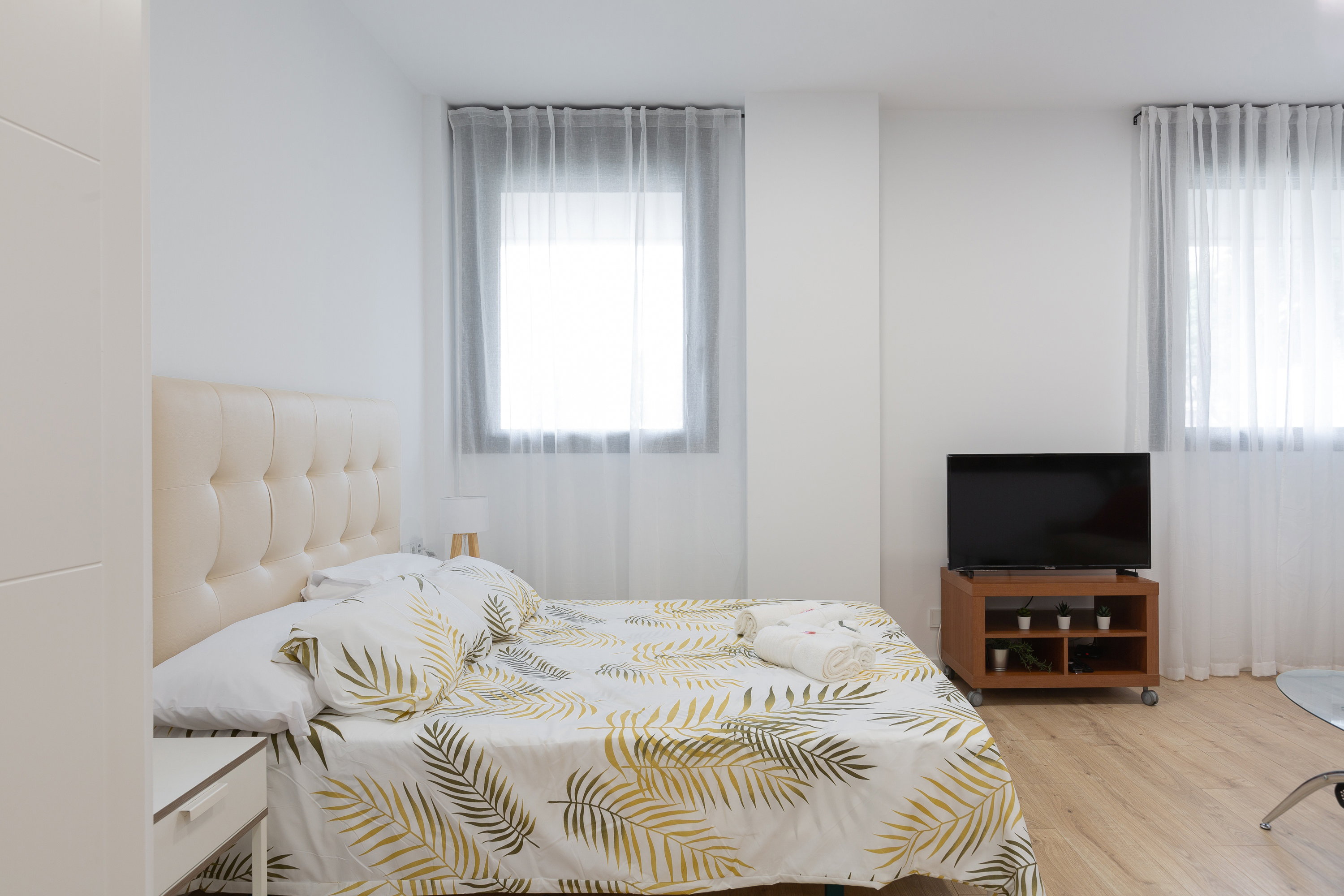 A large double bed with nightstands and a lamp, a window with a curtain, and a TV on the dresser.