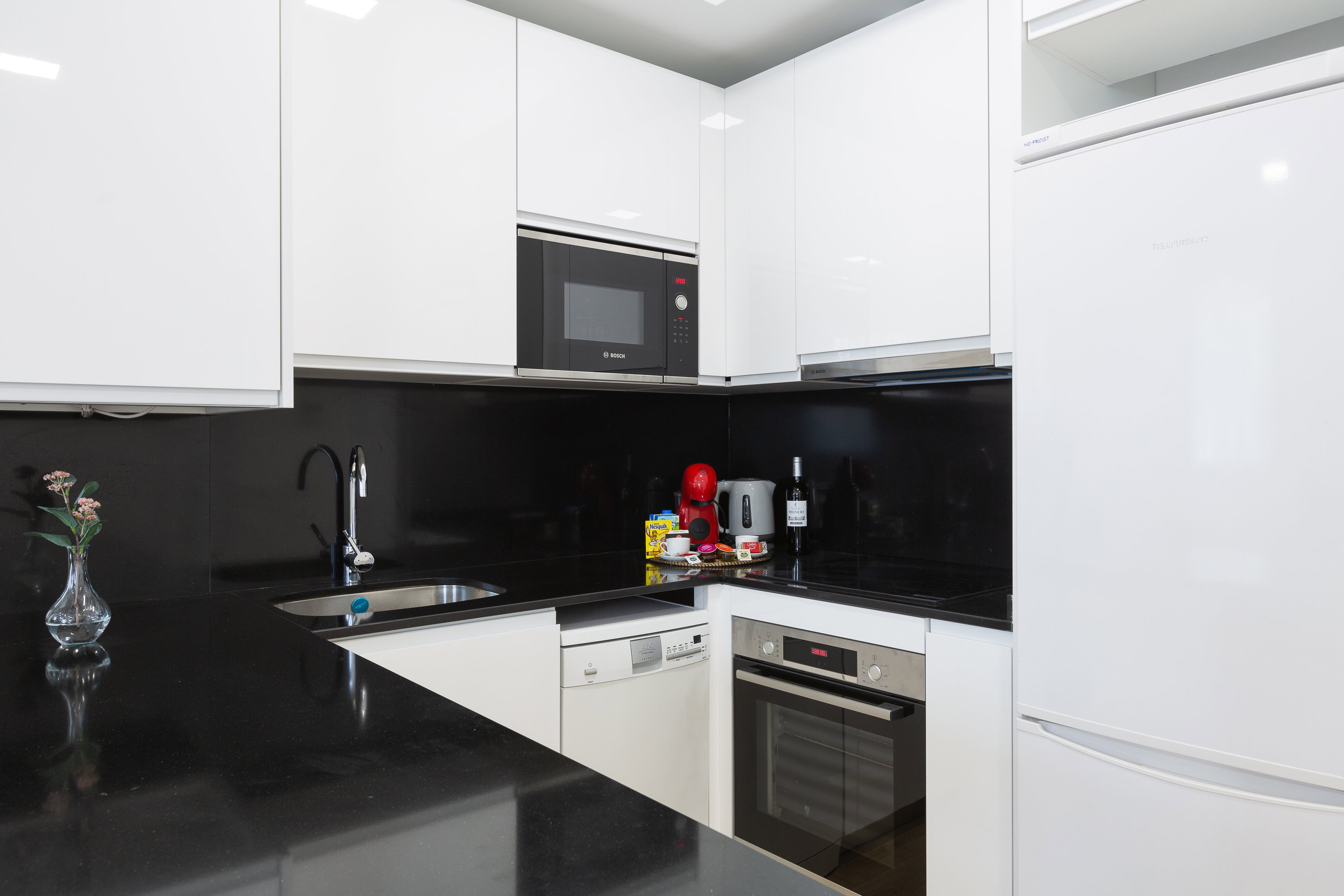 Kitchen interior. Cabinets, sink, dishwasher, oven, microwave, induction hob, hood, kettle, and refrigerator.