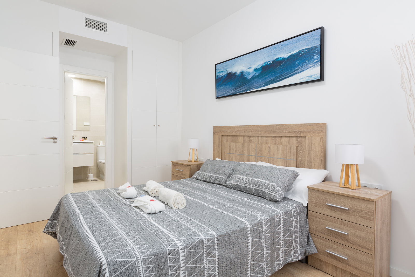 Rest in this serene bedroom with warm wood finishes and coastal art. An adjacent modern bathroom ensures complete comfort.