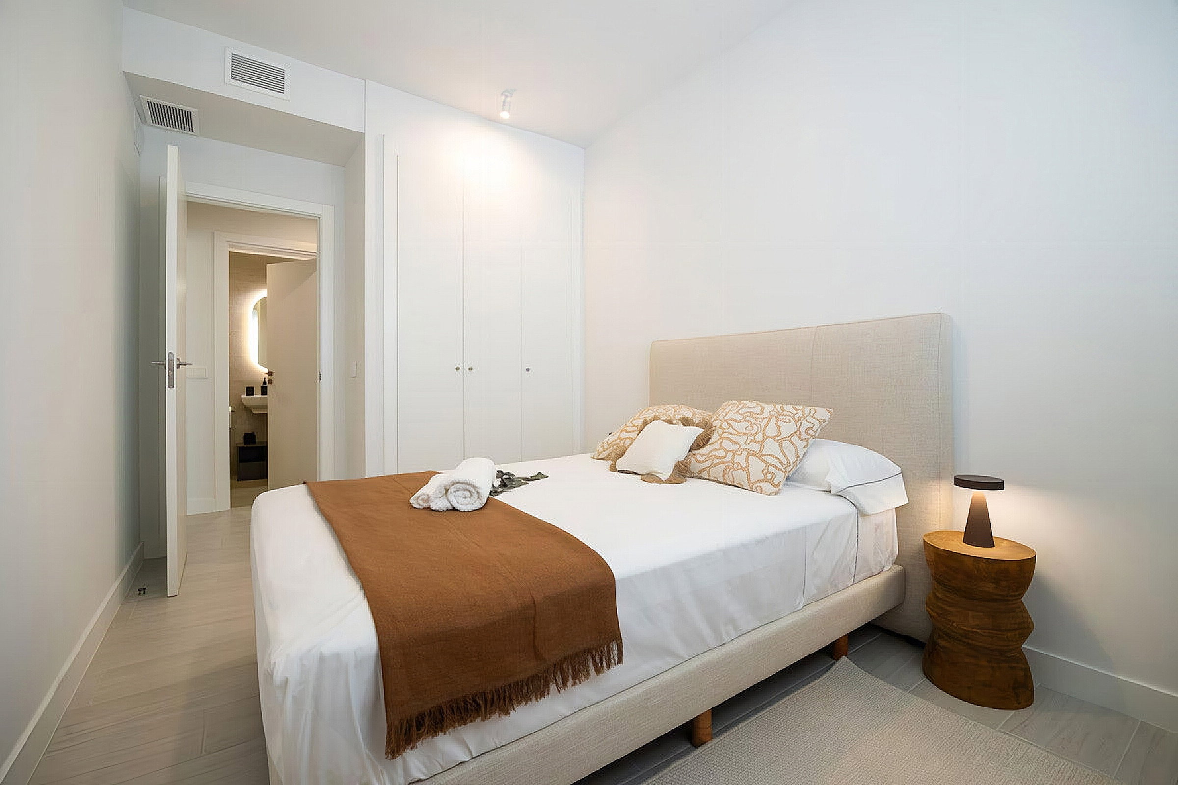 Relax in a serene bedroom with crisp linens and warm wooden accents. A sleek en-suite bathroom awaits just beyond the door.