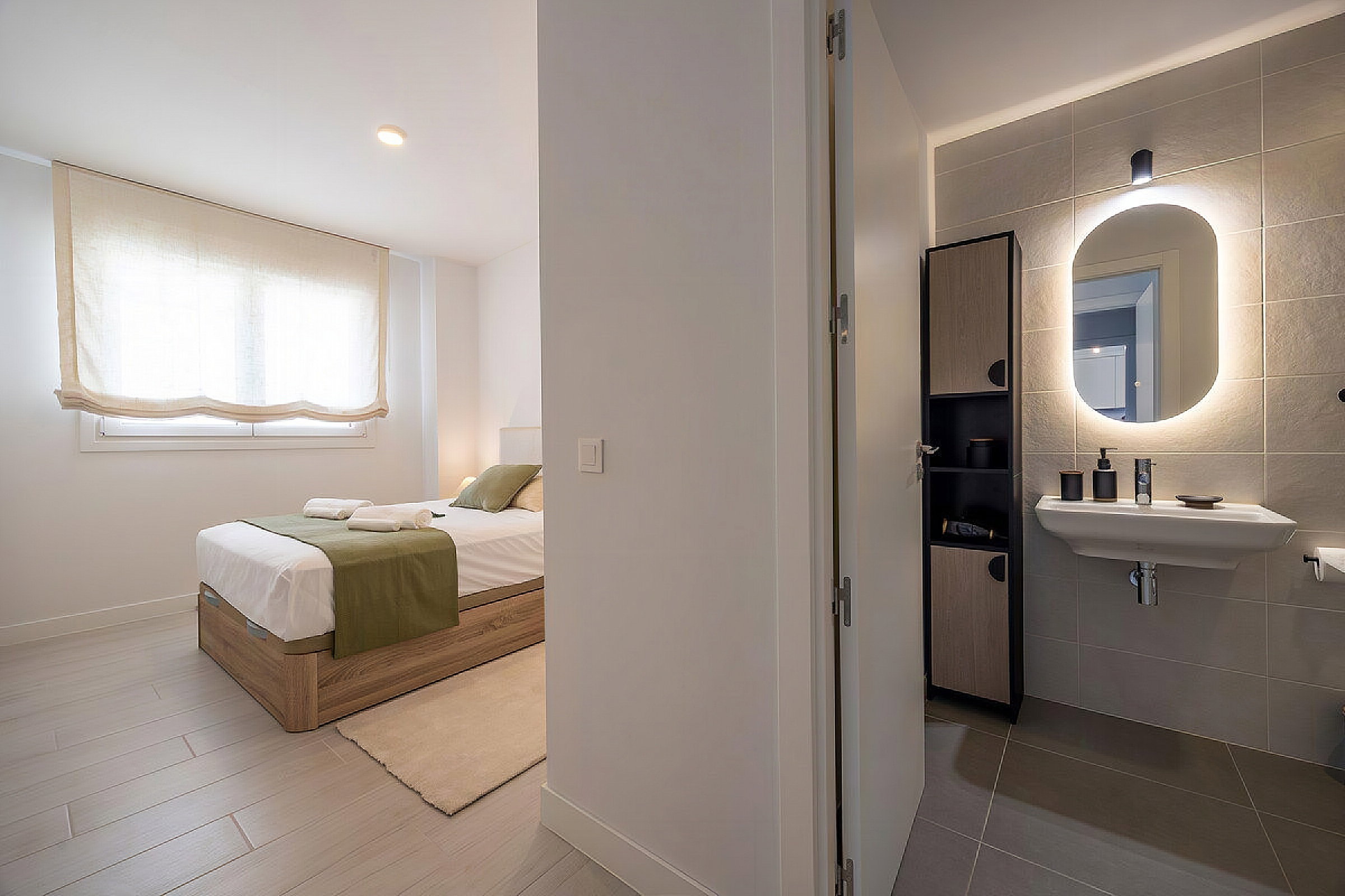This bright bedroom offers a cozy bed and connects to a sleek en-suite bathroom. Note the modern finishes and backlit mirror.