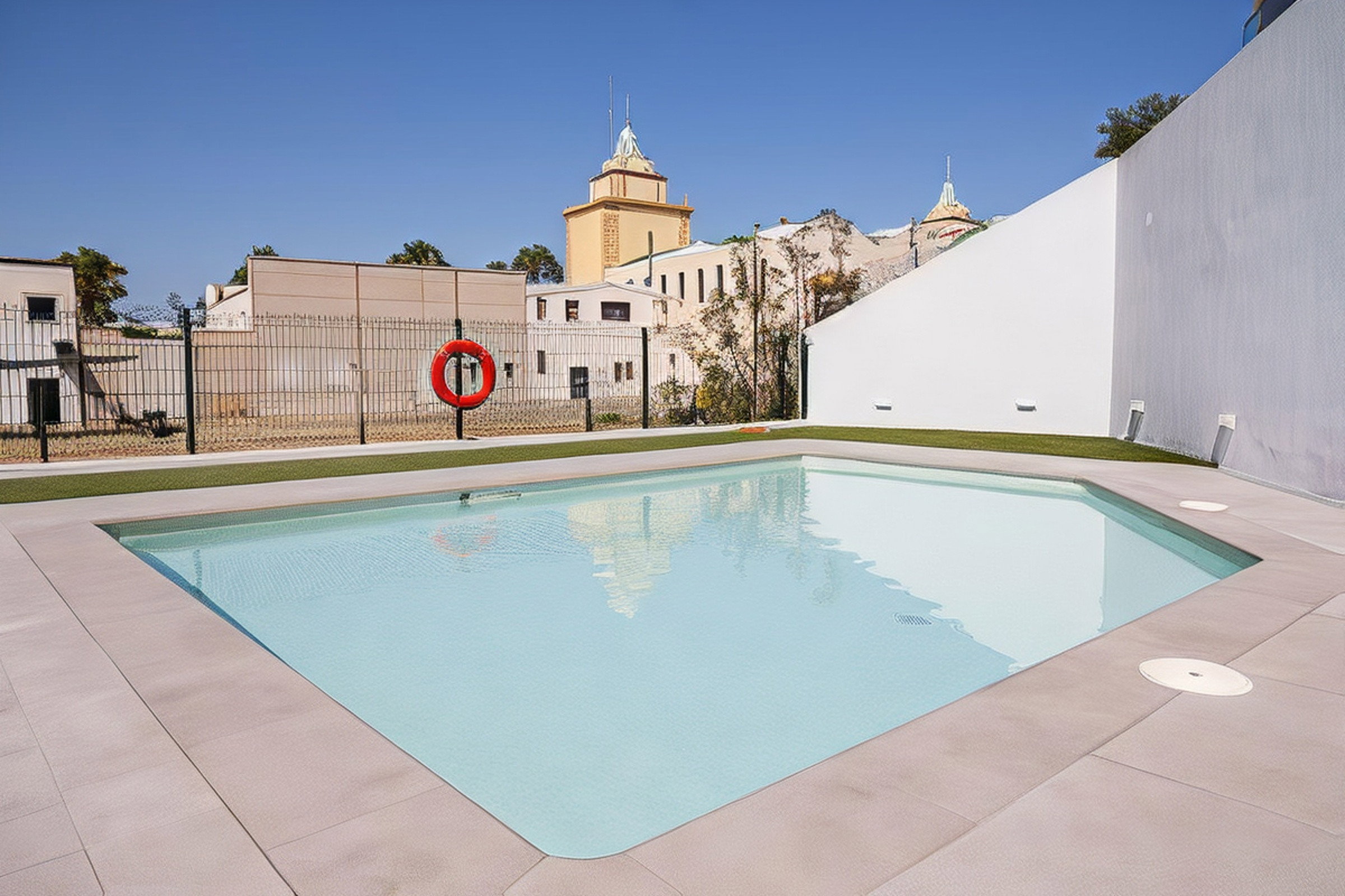 Relax by the pristine communal pool under a bright blue sky. The calm waters perfectly reflect classic Estepona architecture.