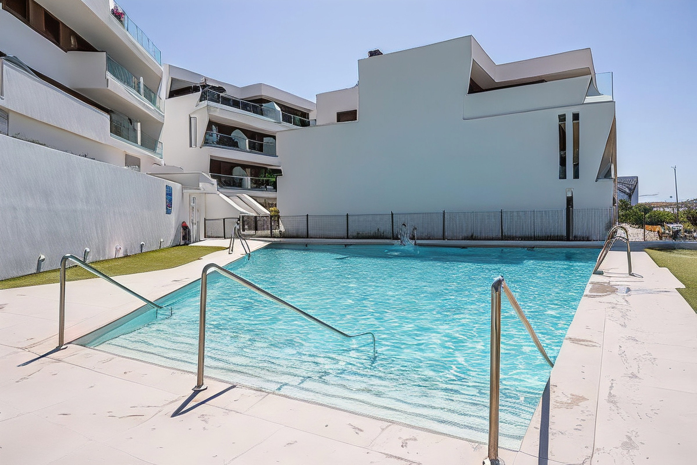A pristine communal pool invites relaxation beneath a clear sky. Modern white architecture frames this peaceful Estepona oasis.