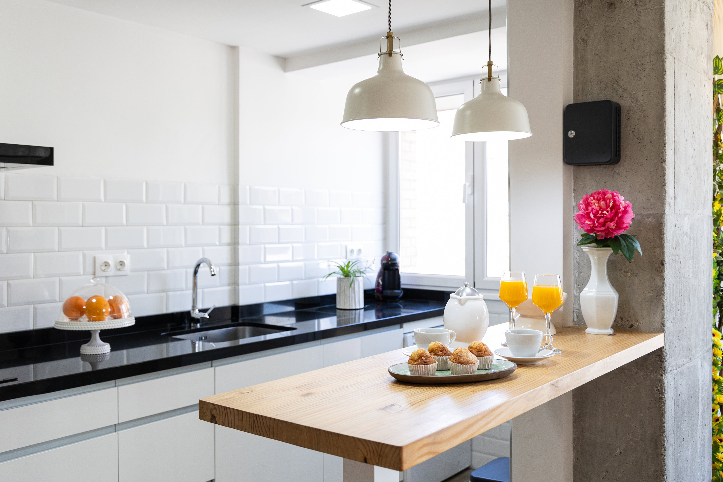 A kitchen with white cabinets, a black countertop, a sink, and a wooden table, with two white pendant lamps above it.