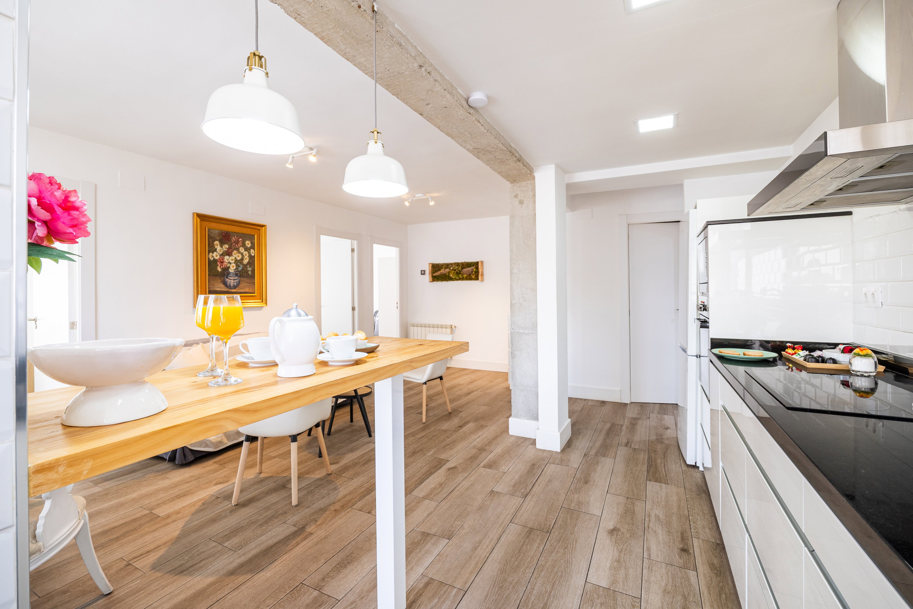 A kitchen with white fronts and a black countertop, with an induction hob combined with a wooden dining table under two large lamps.