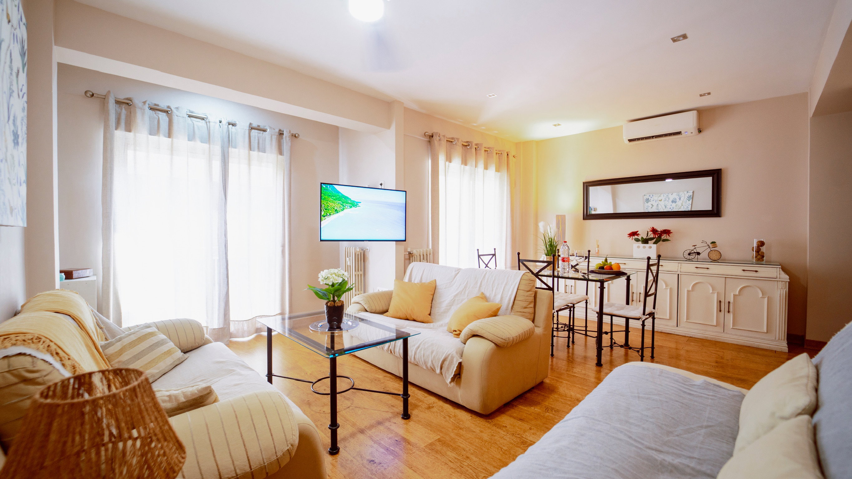 three sofas, coffee table, a TV, mirror hang on the wall, three drawers, dining area with chairs, two large windows with curtainst, Radiators, air conditioning.