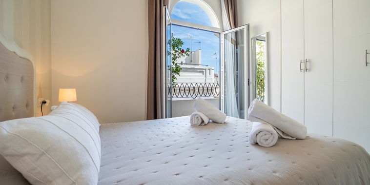 Sunlight fills this elegant bedroom through an arched balcony door. Fresh linens and rolled towels await your relaxing stay.